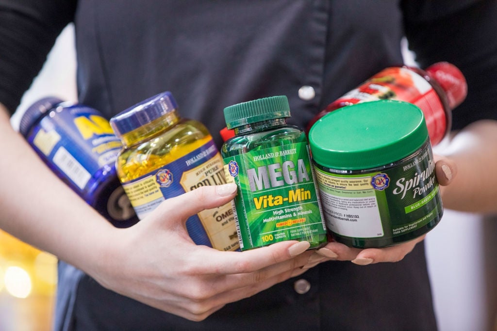 Person holding assorted  supplement bottles, including Mega Vita-Min and food  oil, showcasing wellness  and wellness products