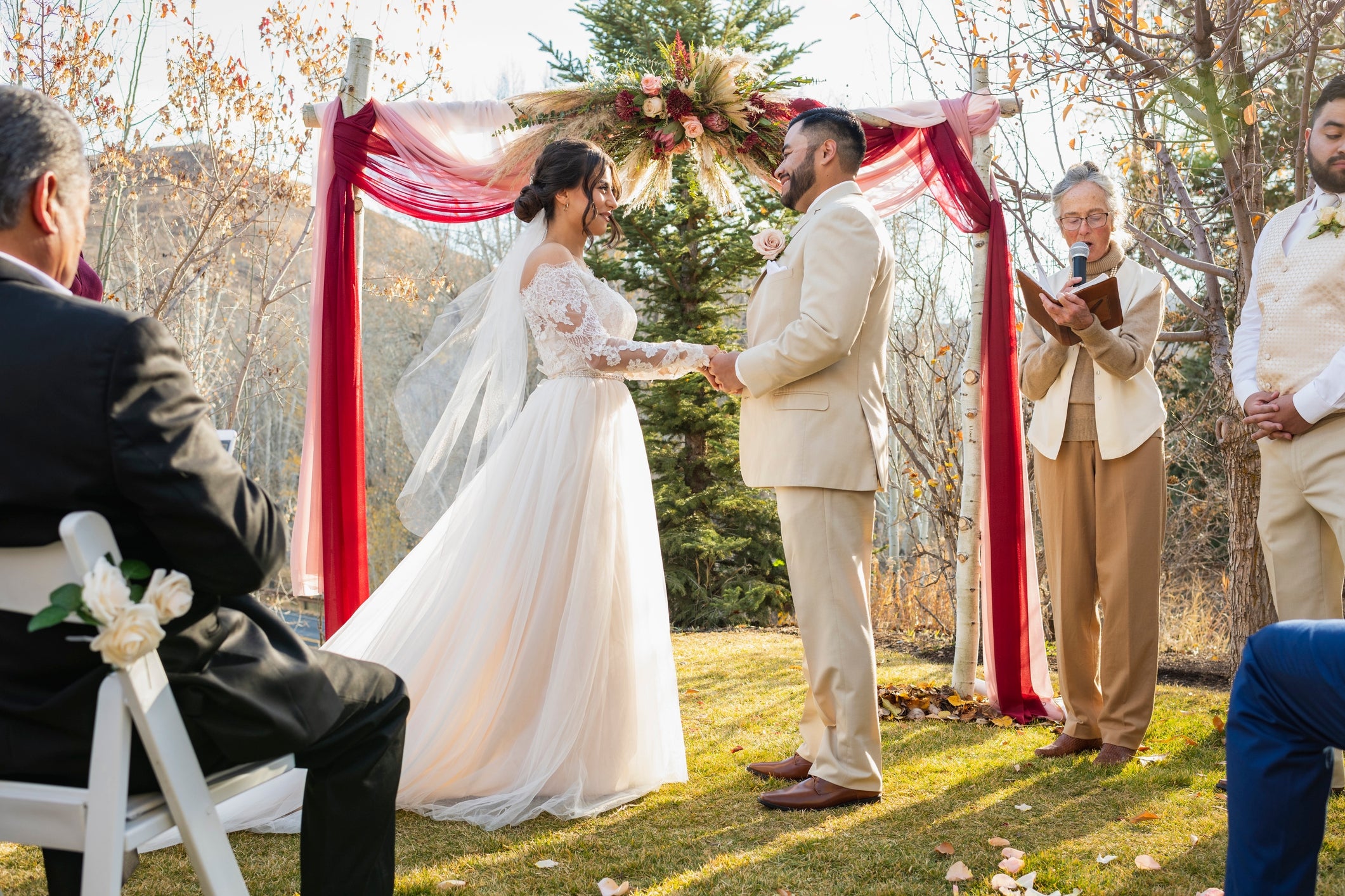 A mates  exchanges vows outdoors nether  a decorated arch during a wedding ceremony, surrounded by a tiny  radical  of guests