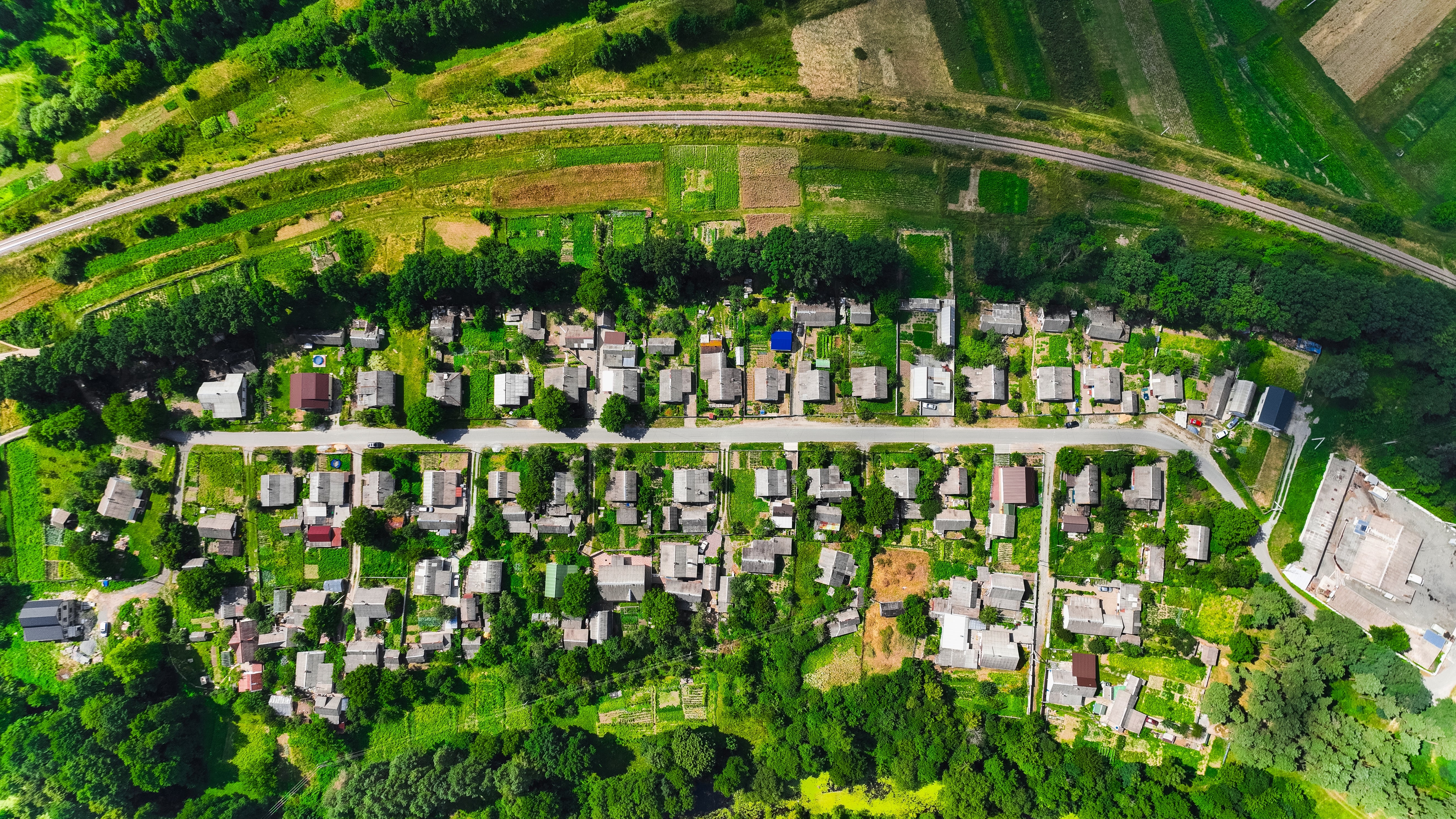 Aerial view of a suburban neighborhood with houses, roads, and greenery, bordered by a railway track