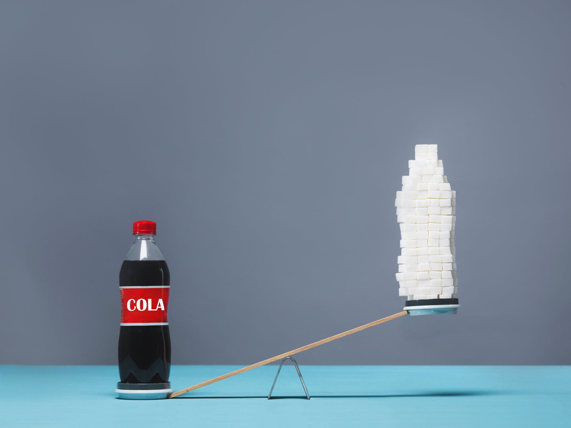 Soda vessel  connected  1  broadside  of a seesaw, stack of sweetener  cubes connected  the other, indicating sweetener  contented  comparison