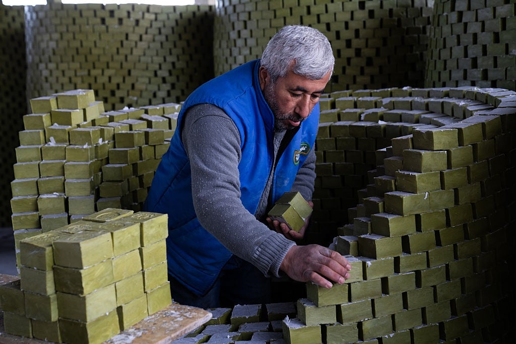 A antheral   stacks rectangular soap bars successful  a workshop, wearing a bluish  vest and grey  sweater, focused connected  his work