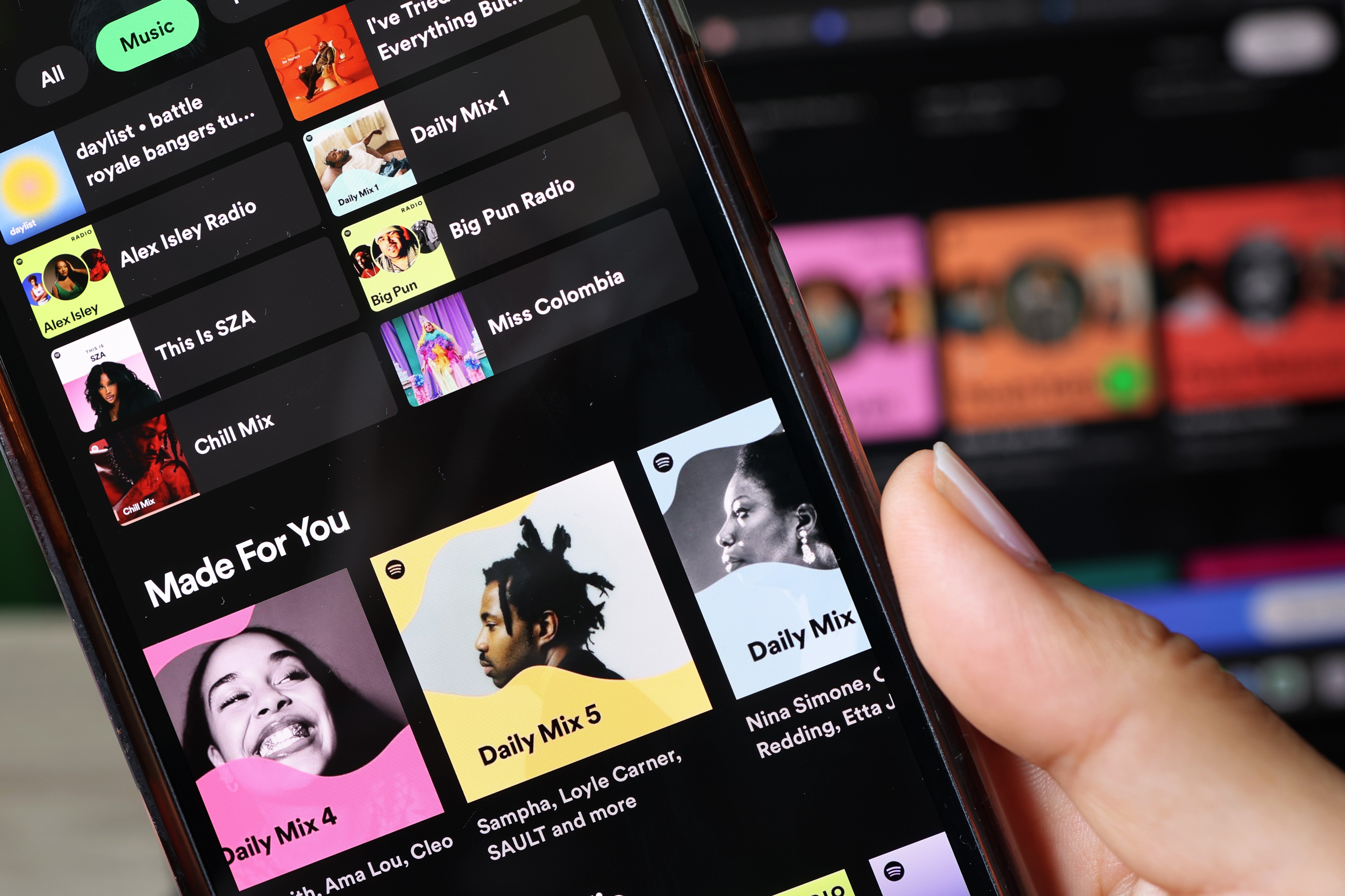Close-up of a manus  holding a smartphone displaying Spotify playlist suggestions, including Daily Mixes and creator  recommendations