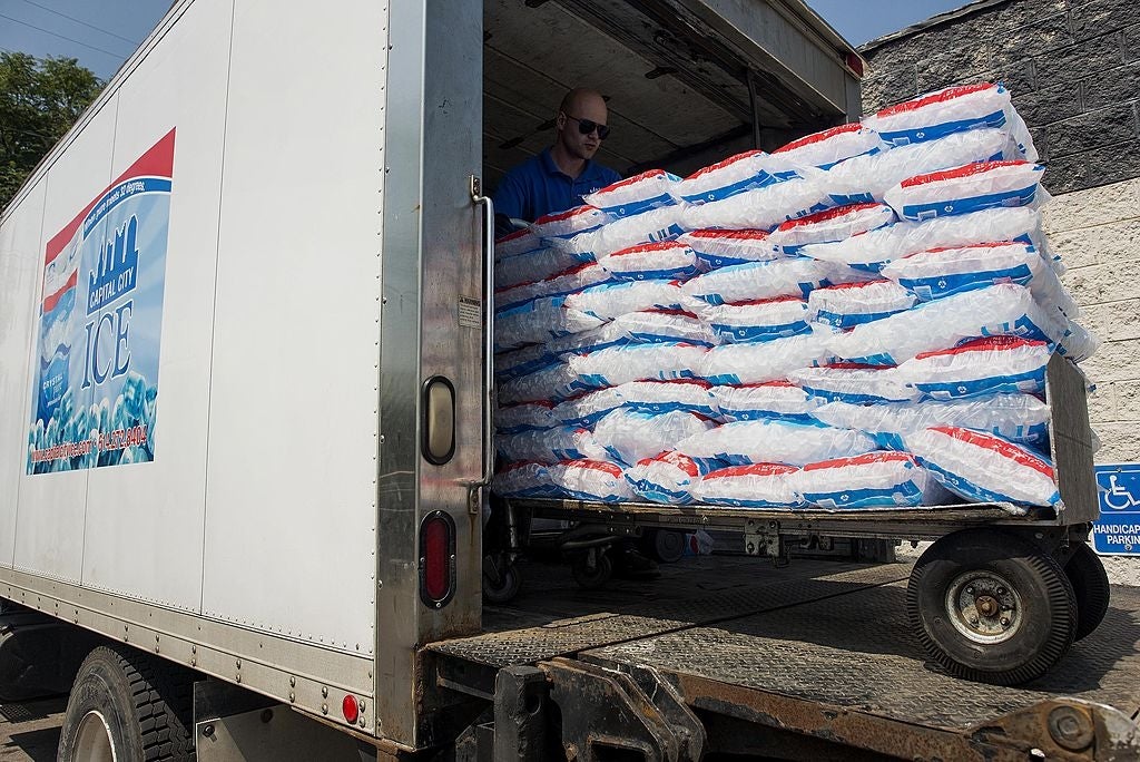 A idiosyncratic    unloads a motortruck  filled with bags of ice, adjacent  to a motion   indicating a handicapped parking spot