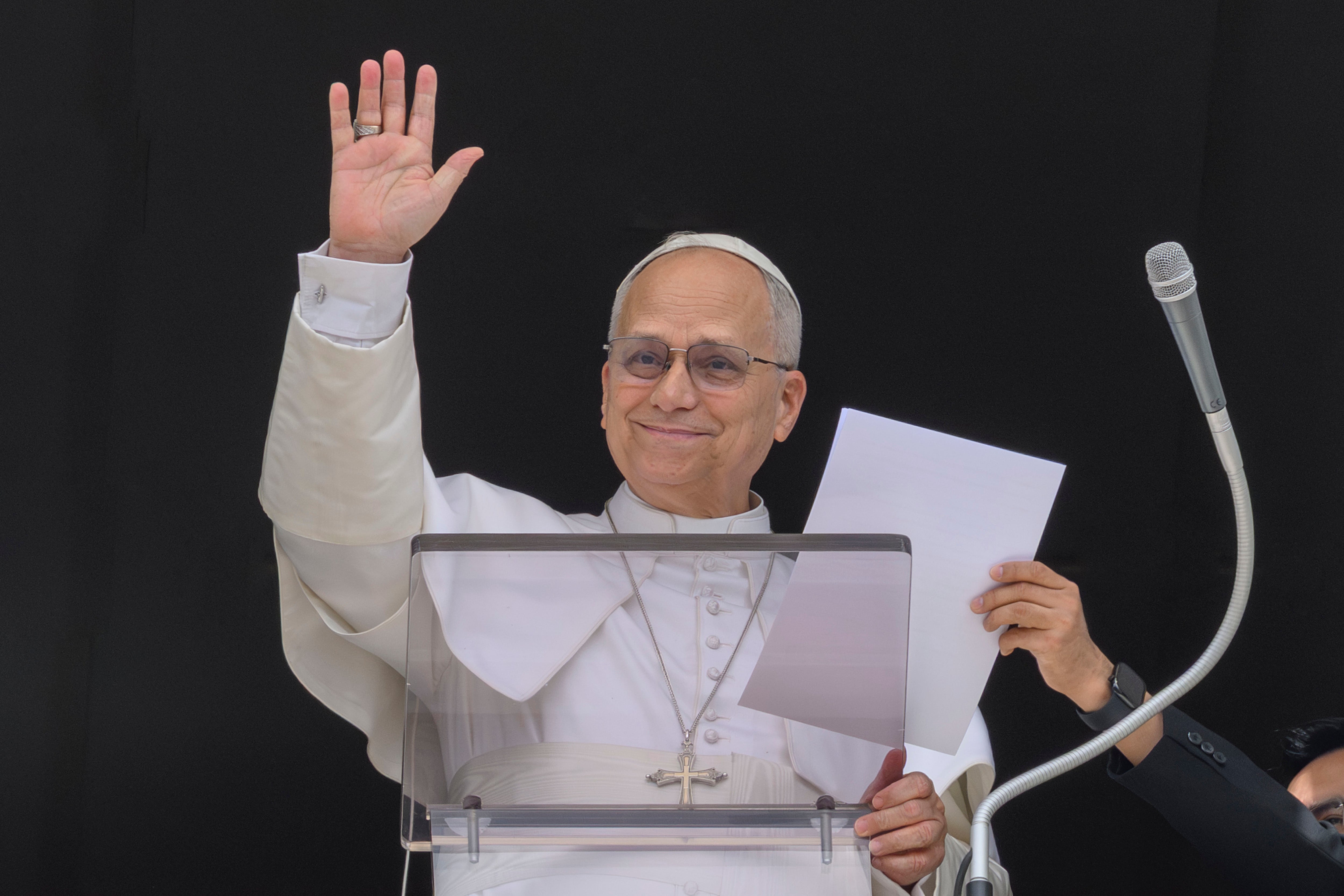 A idiosyncratic   wearing spiritual  attire waves portion    holding a insubstantial  down  a podium with a microphone