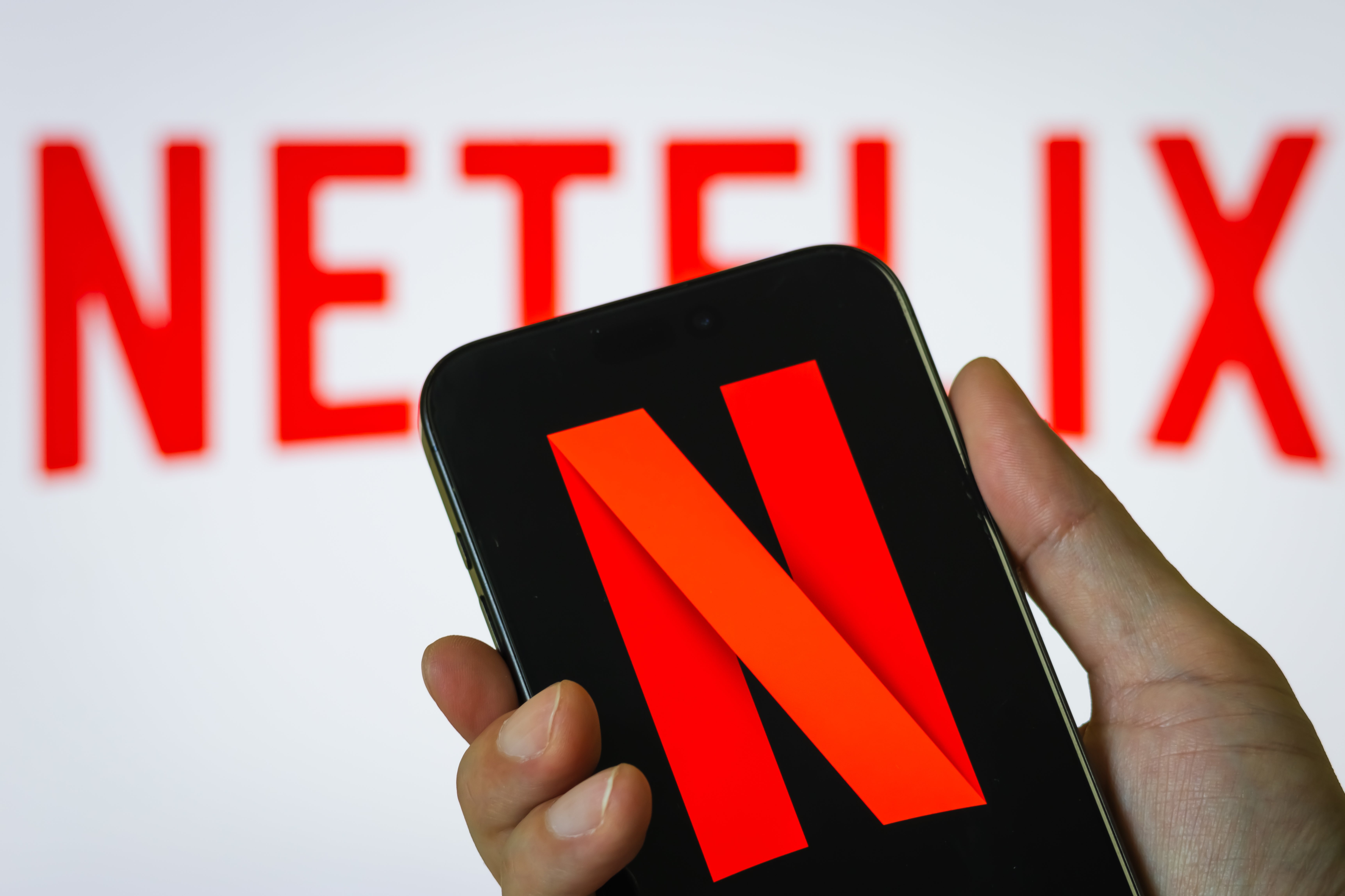 Person holding a smartphone displaying the Netflix logo, with a larger Netflix motion   successful  the background