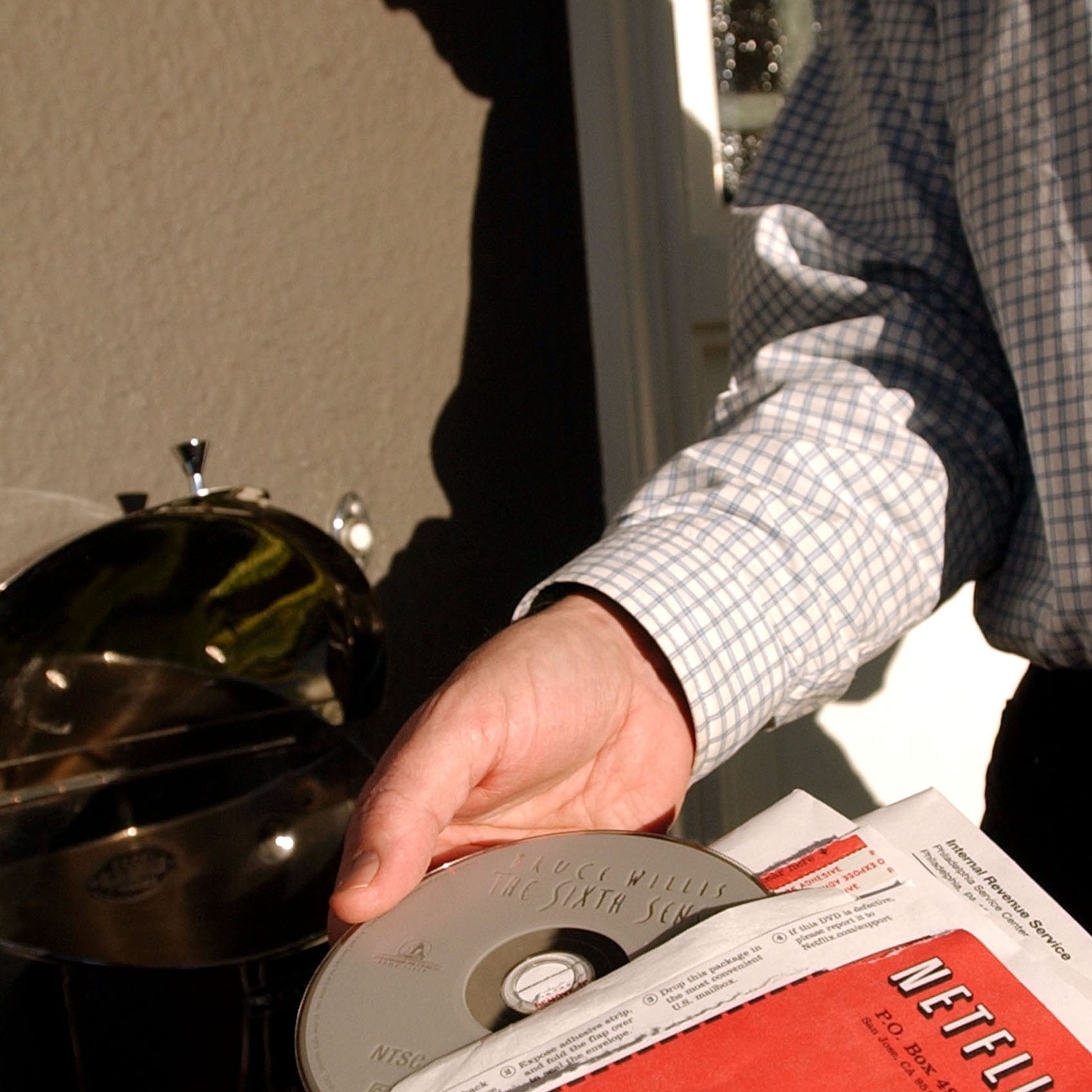 Person inserting a Netflix DVD envelope into a mailbox, capturing a nostalgic infinitesimal   from the DVD rental era