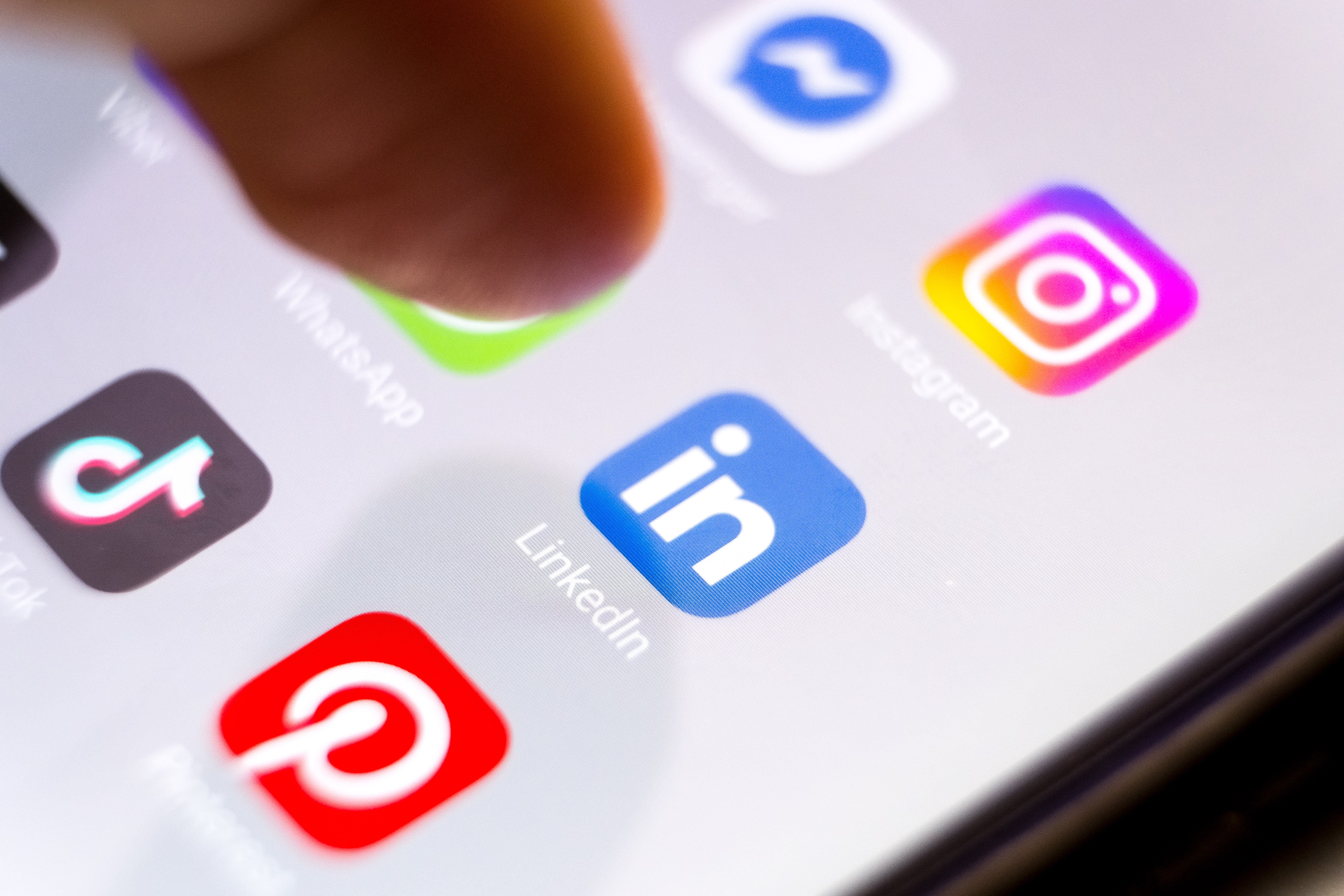 Smartphone surface  with societal  media app icons, including Instagram, WhatsApp, LinkedIn, TikTok, Pinterest, and Messenger, being tapped