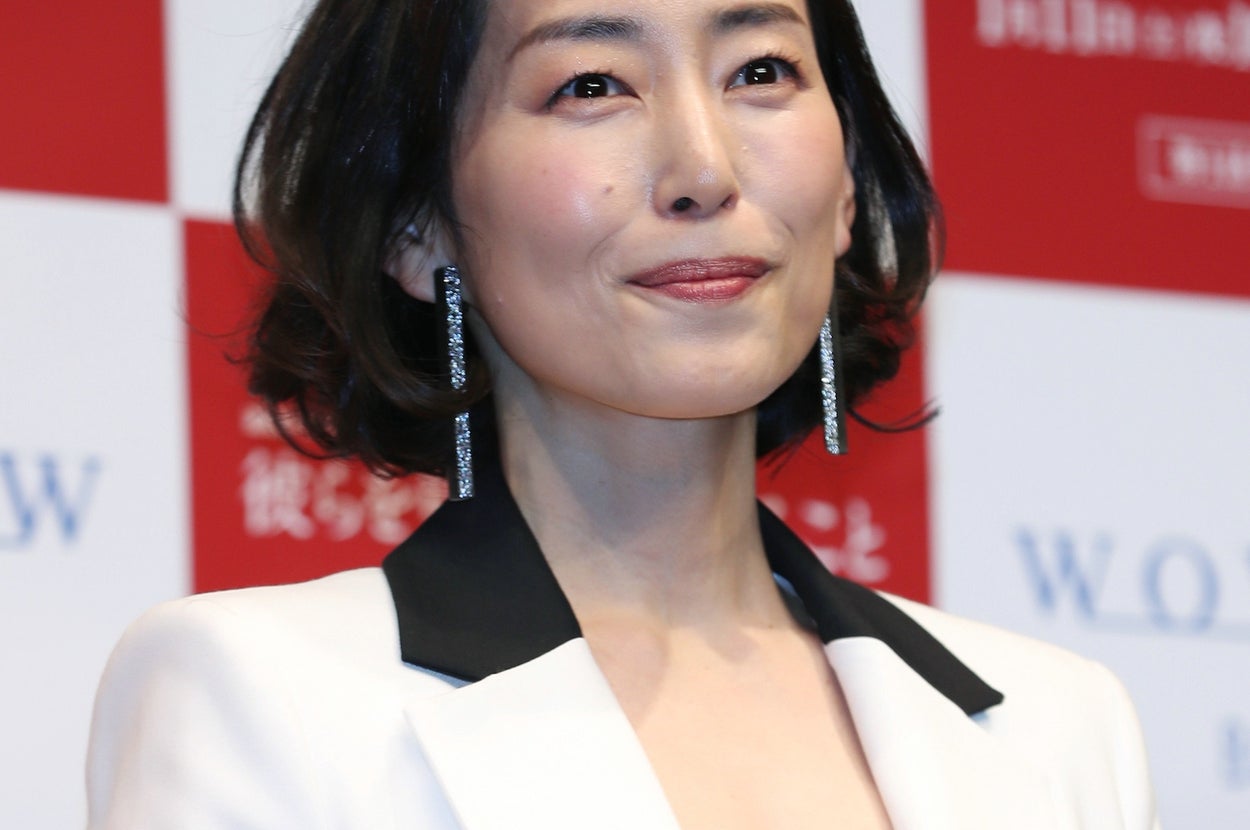 有名人がジャケットとイヤリングを身につけ、イベントでポーズを取っている。背景にはロゴが見える。