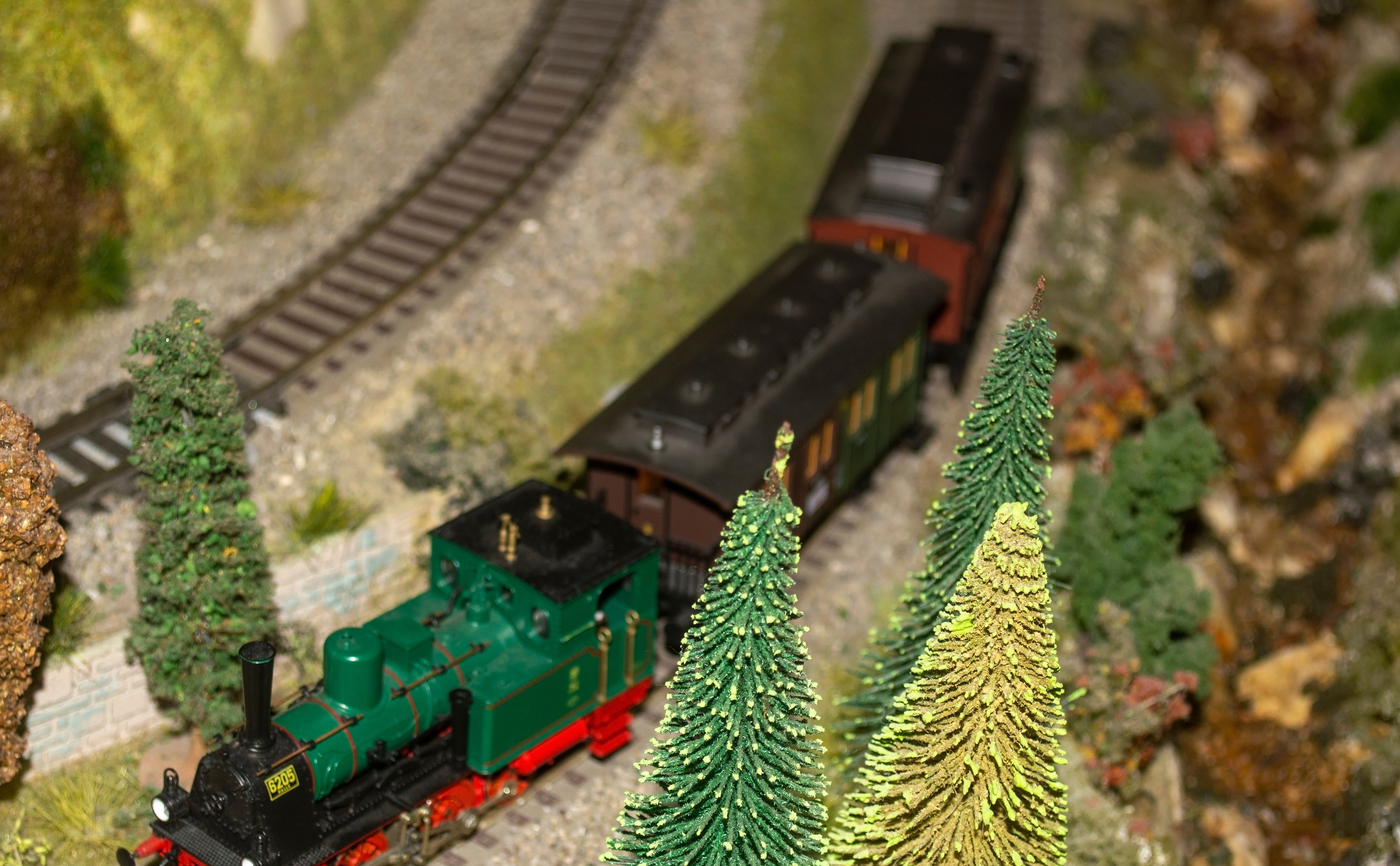 Model bid     acceptable   with a tiny  greenish  locomotive traveling done  a miniature scenery  with trees and elaborate  terrain