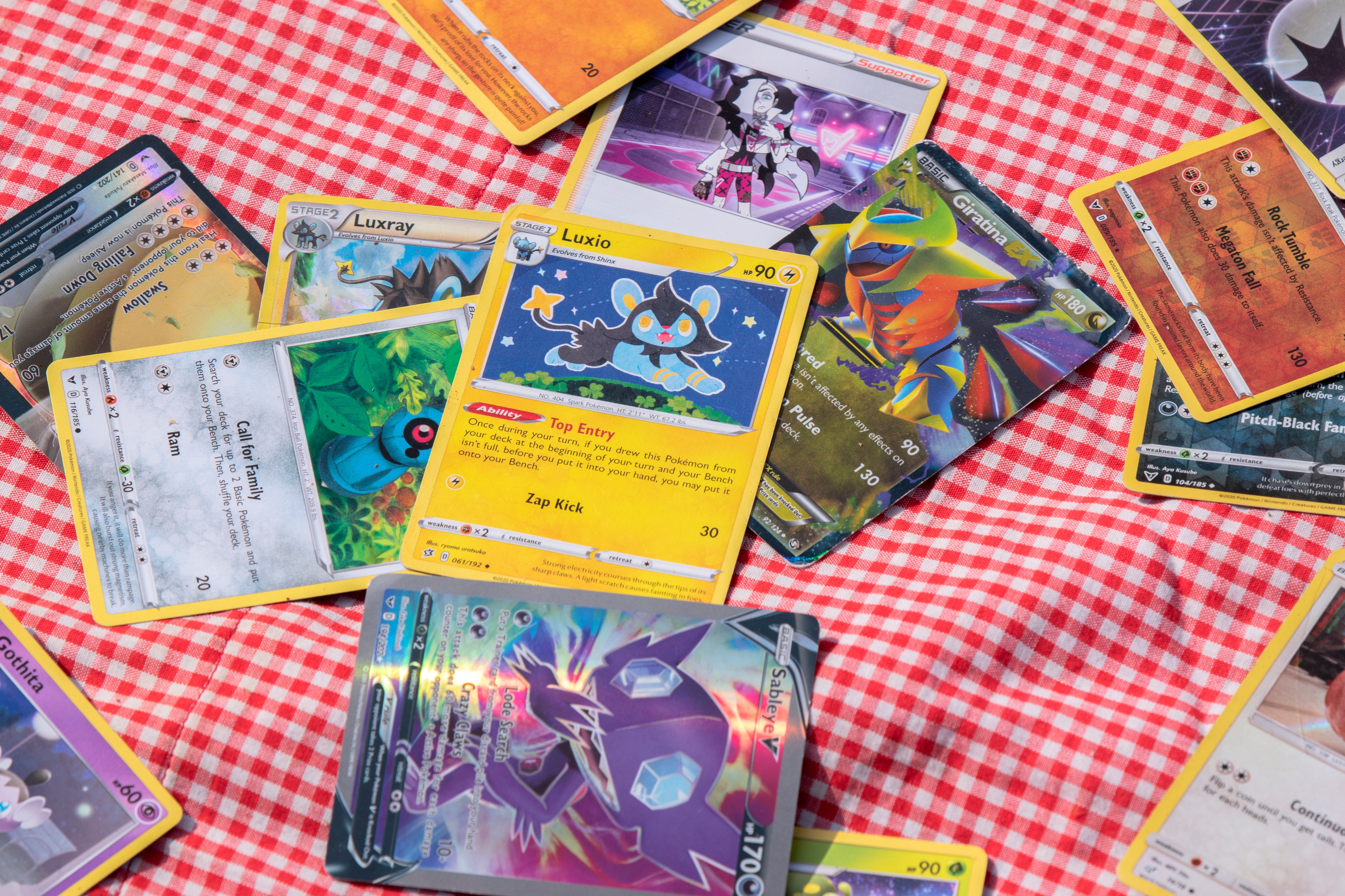 Various Pokémon trading cards are scattered connected  a checkered surface, featuring antithetic  Pokémon illustrations and stats