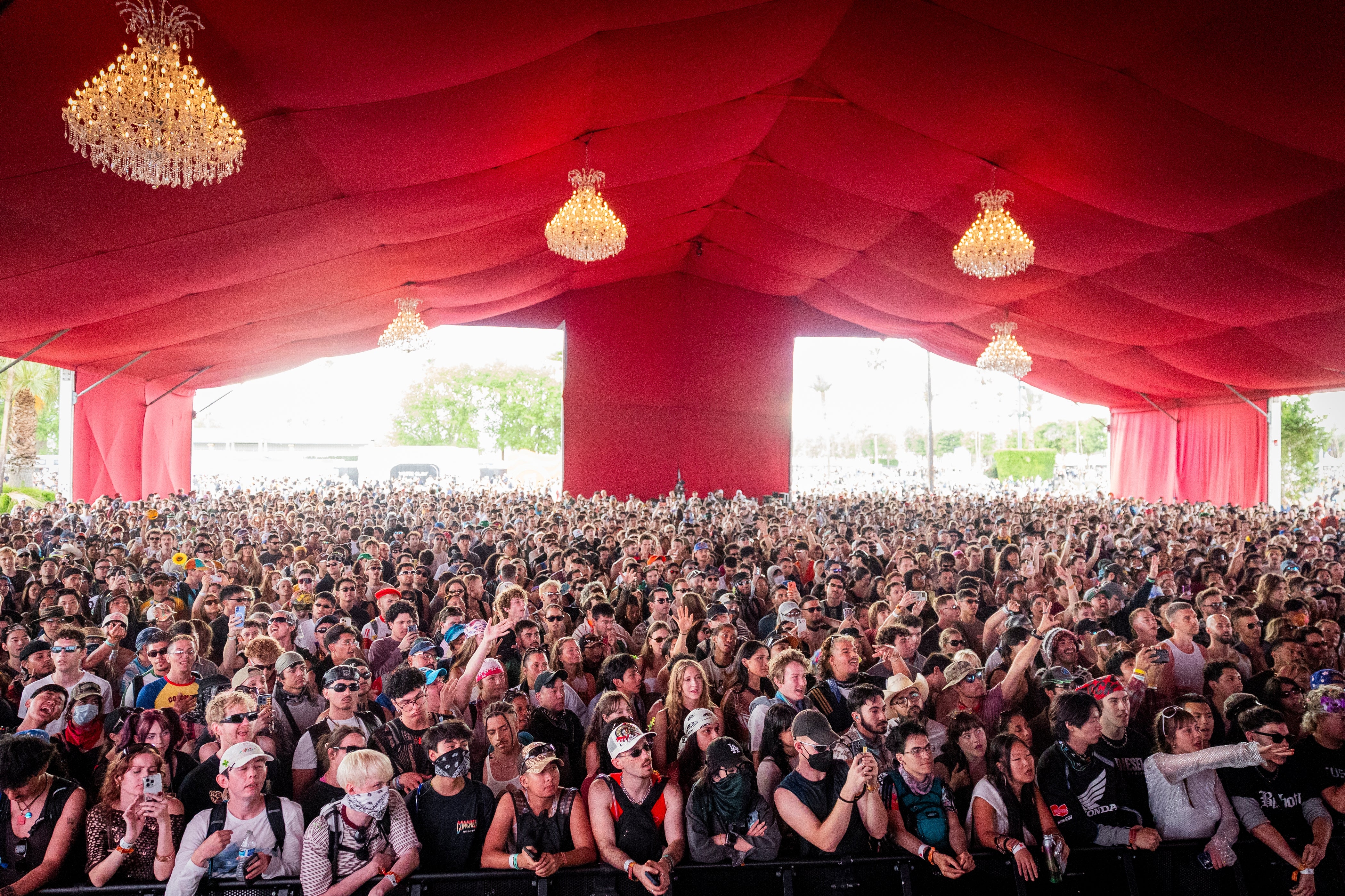 Large festival assemblage  nether  a reddish  canopy, facing the stage, with chandeliers hanging above
