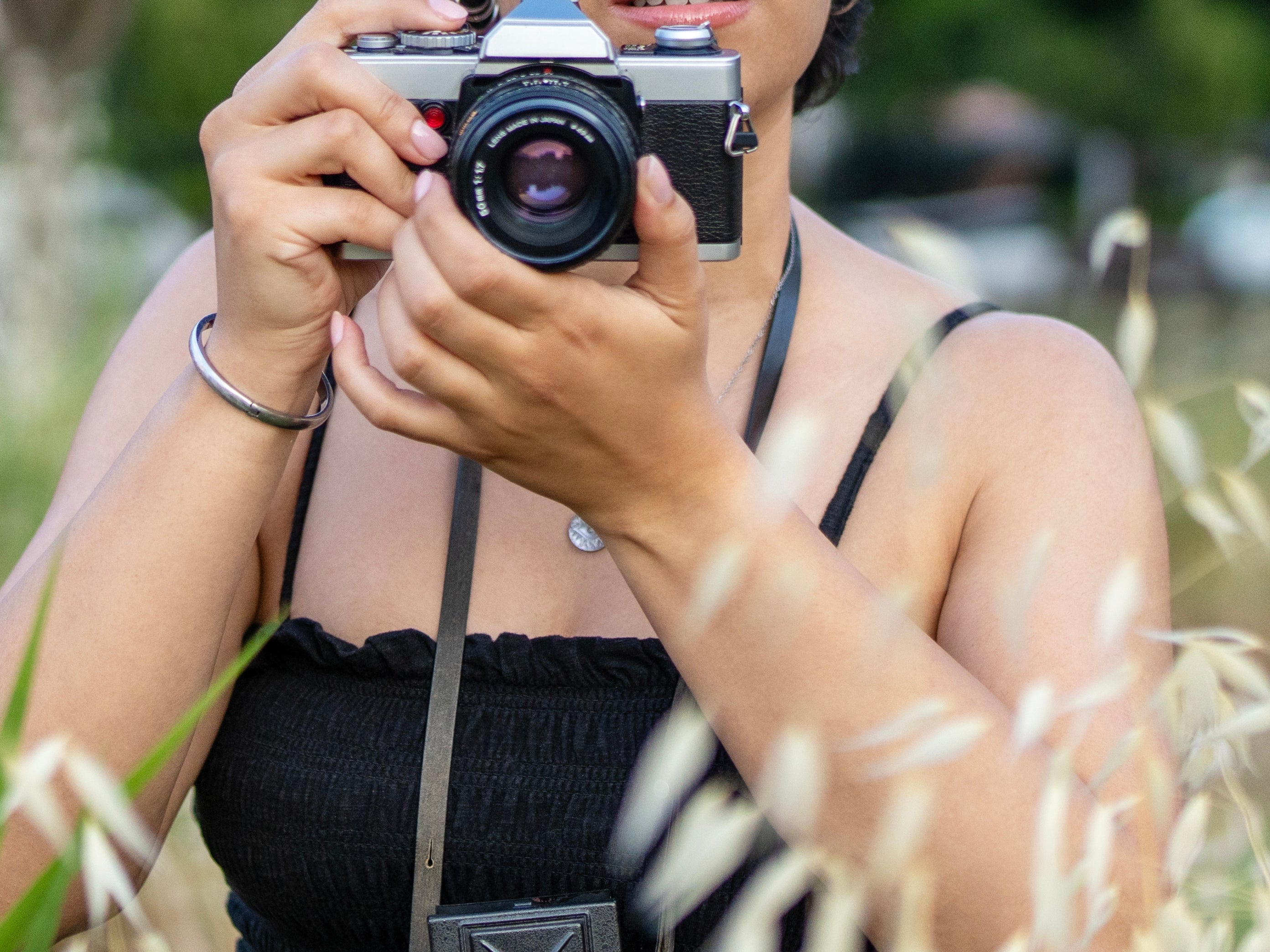 Person with a vintage camera successful  a field, wearing glasses and a sleeveless dress, surrounded by plants