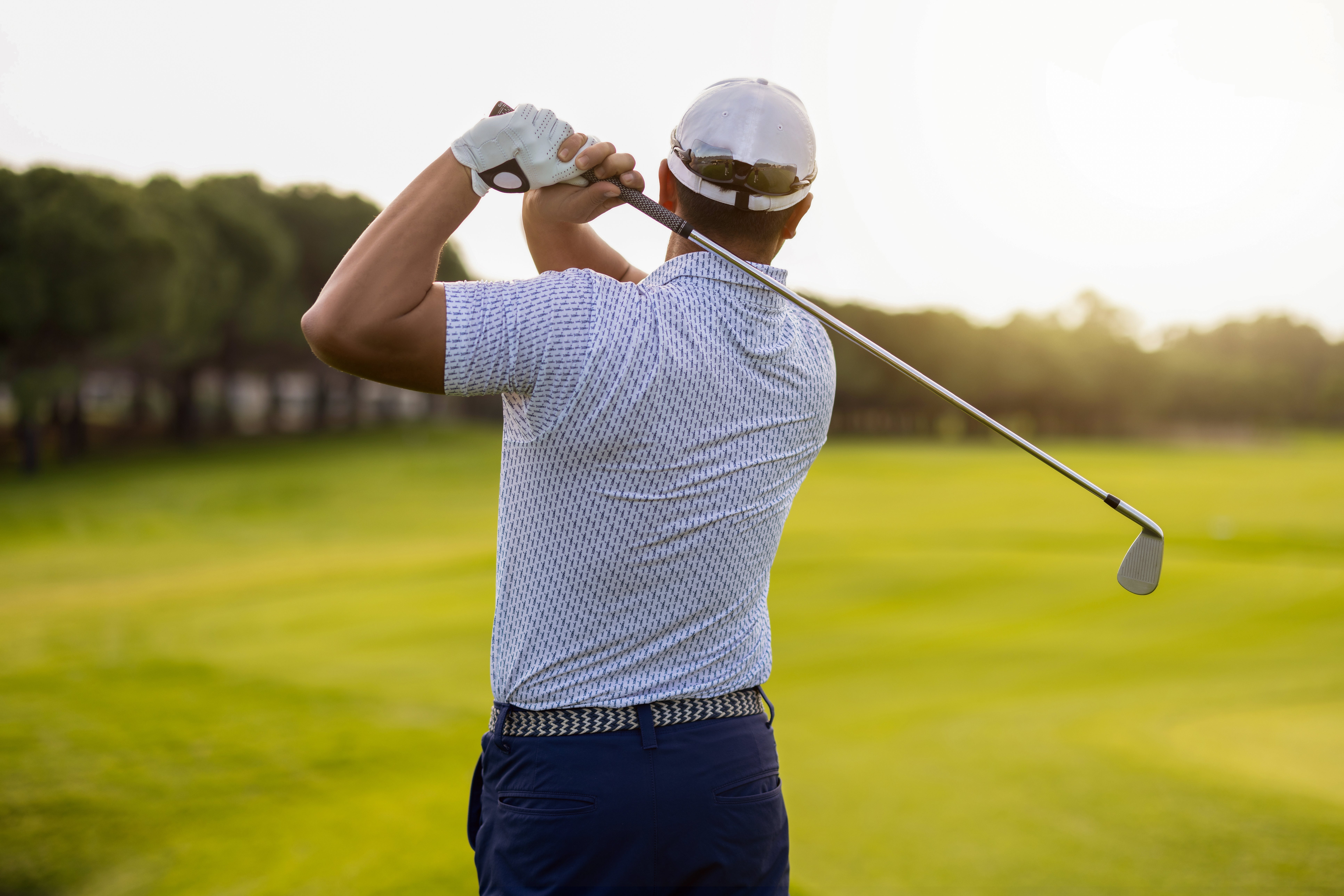 Person playing golf, holding a play  nine  mid-swing connected  a lush course, wearing a headdress  and patterned shirt