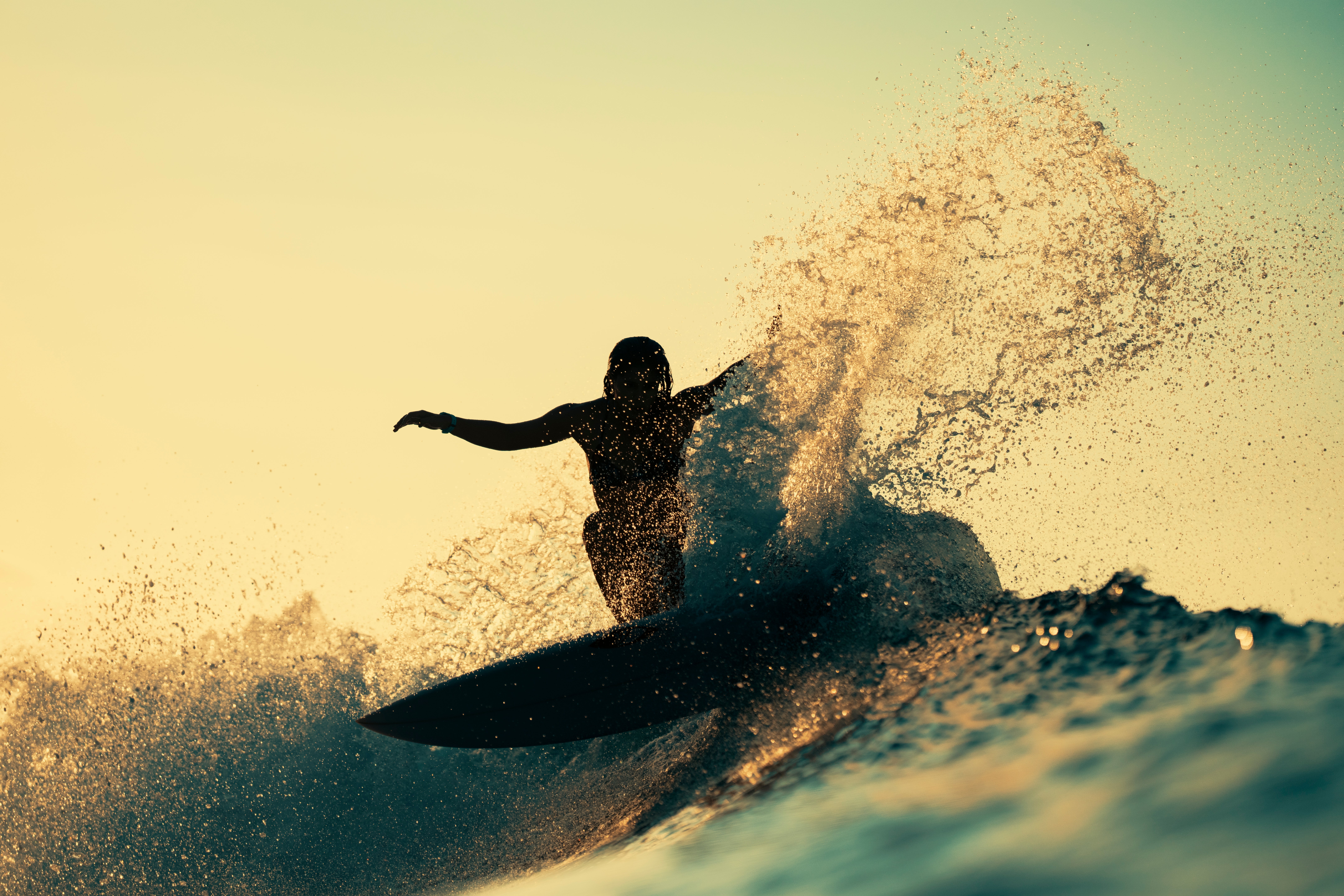 Silhouette of a surfer riding a wave, with h2o  splashing dramatically astir   them successful  a dynamic pose, against a sky