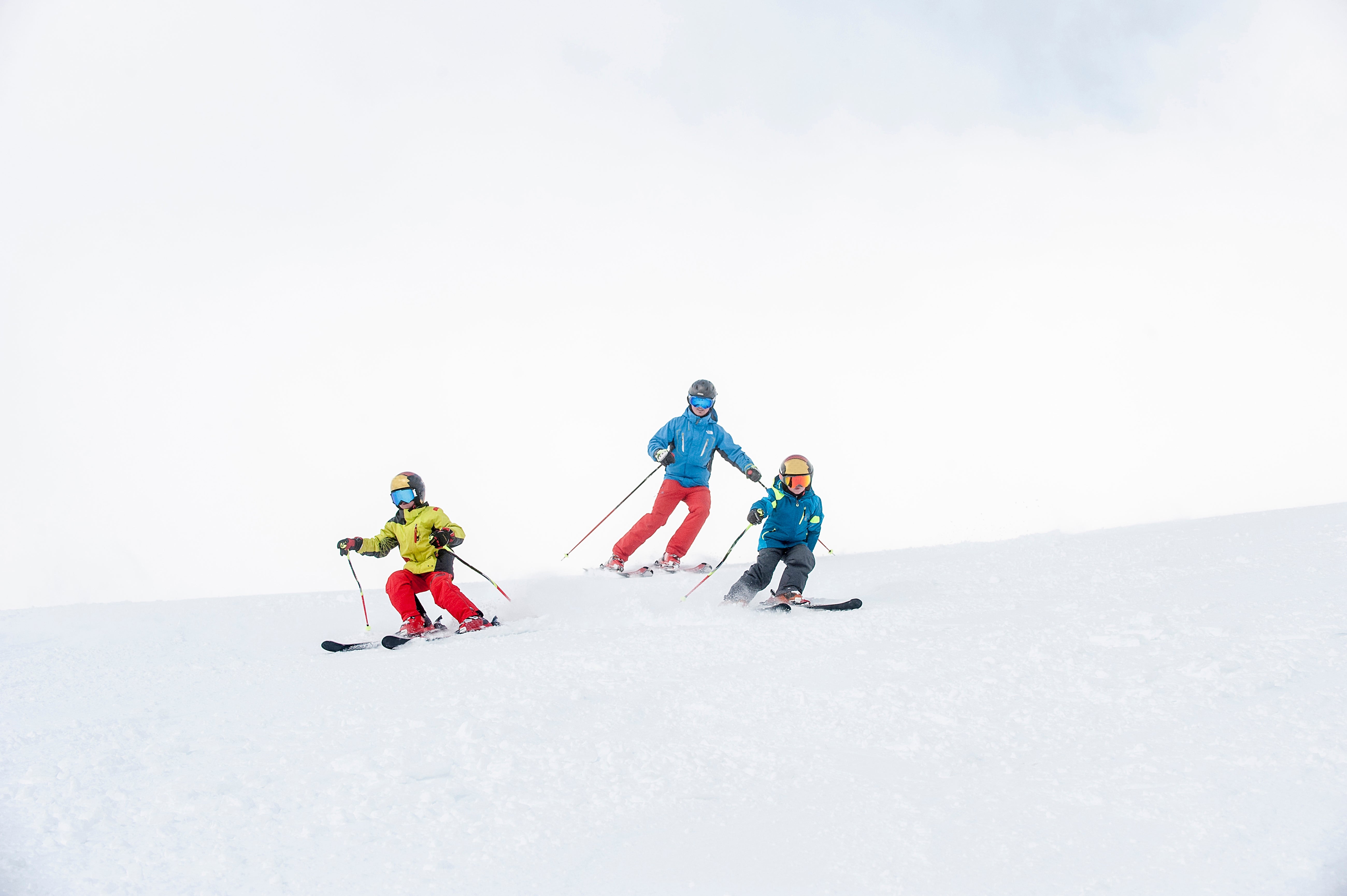 Three skiers descend a snowy slope, wearing helmets and skis  gear, with snowfall  swirling astir   them