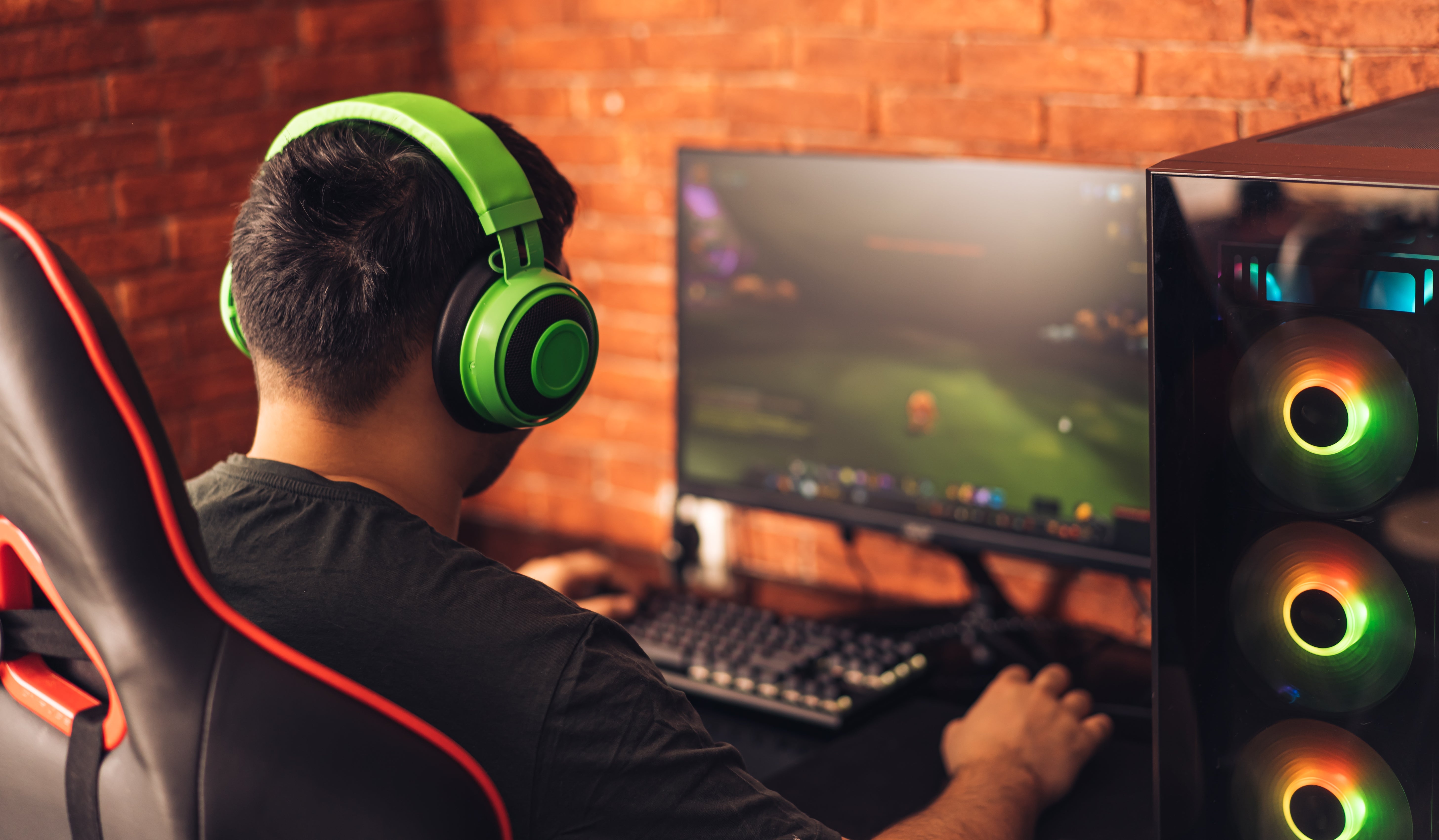 Person wearing headphones playing a video crippled  connected  a computer, seated successful  a gaming chair, with a gaming PC disposable   to the side