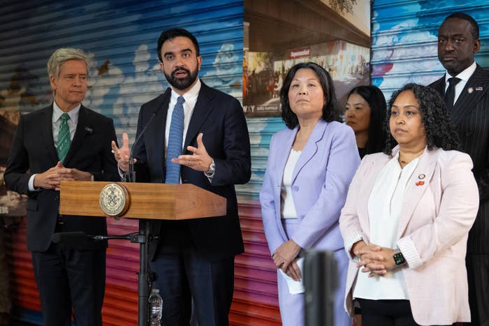 A radical  of officials stands down  a podium during a property   event. One antheral   is speaking, and others, dressed successful  concern  attire, perceive  attentively