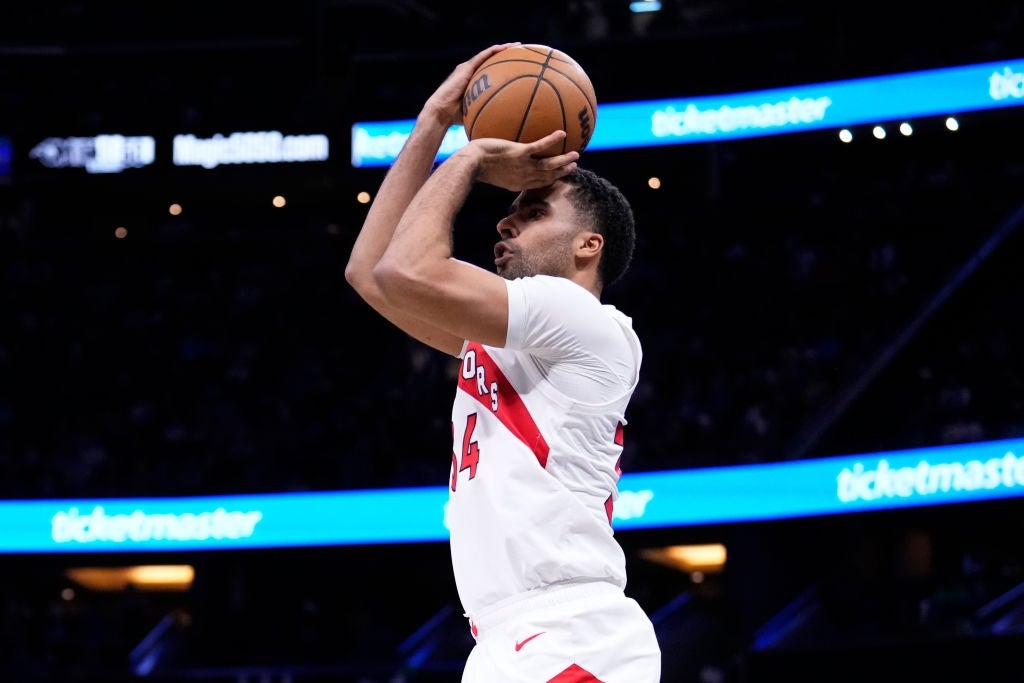 Basketball subordinate    wearing a jersey jumps to sprout  the shot  during a game, with the arena and integer  advertisement banners disposable   successful  the background