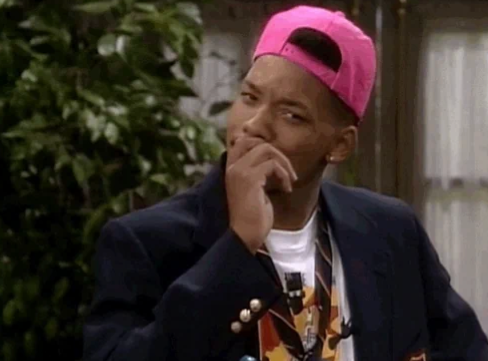 Person successful  a blazer and cap, appearing thoughtful, with manus  adjacent   mouth. Indoor mounting  with plants successful  the background