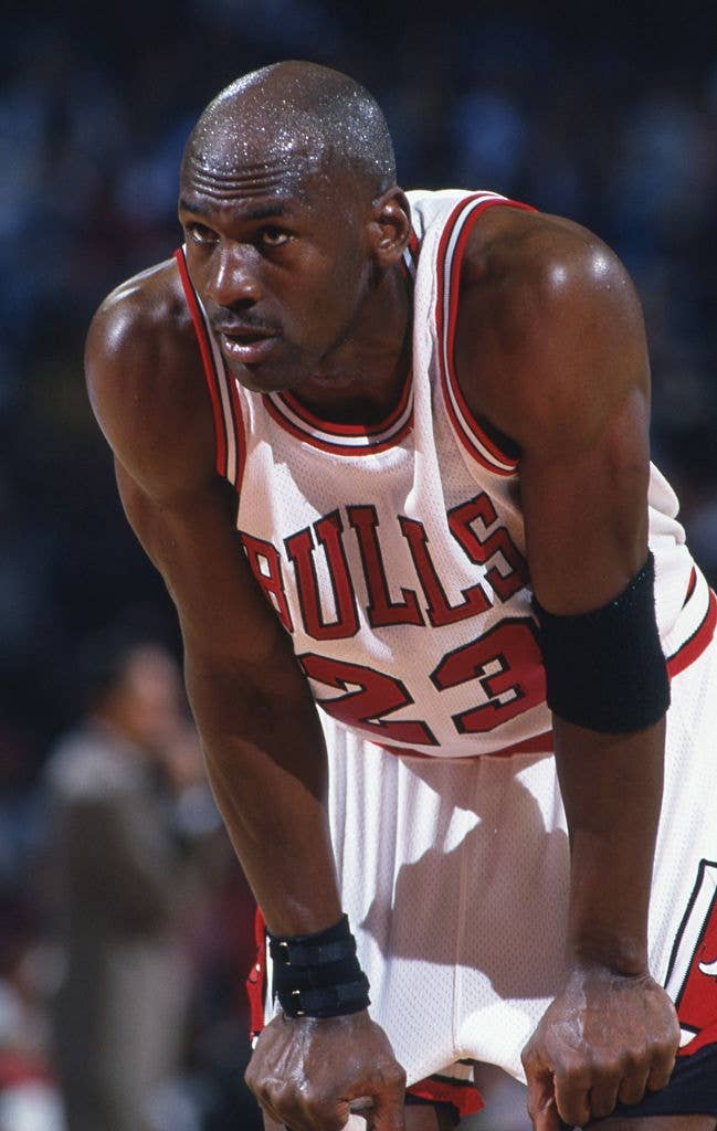 Basketball subordinate    successful  a Bulls jersey, fig   23, leans guardant  with hands connected  knees, appearing focused during a game