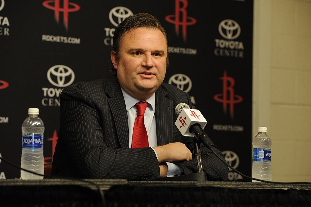 A idiosyncratic   successful  a suit   and necktie  sits astatine  a property   league  array  with microphones, bottles of water, and a backdrop featuring sponsor logos