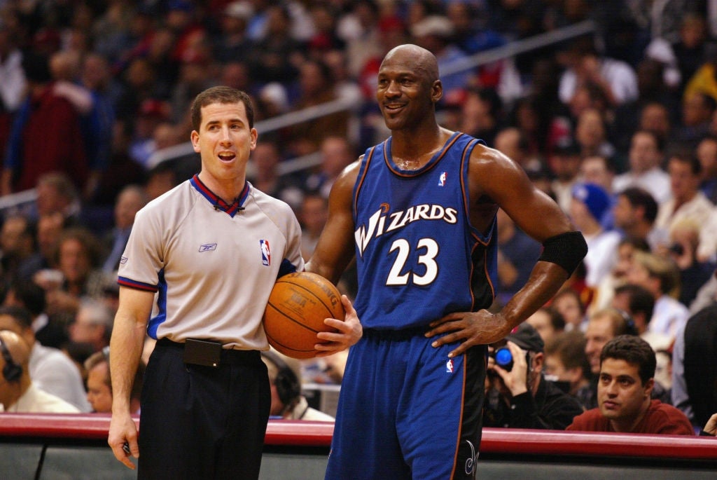 A hoops  subordinate    successful  a Wizards jersey smiles adjacent  to a referee holding a hoops  during a game