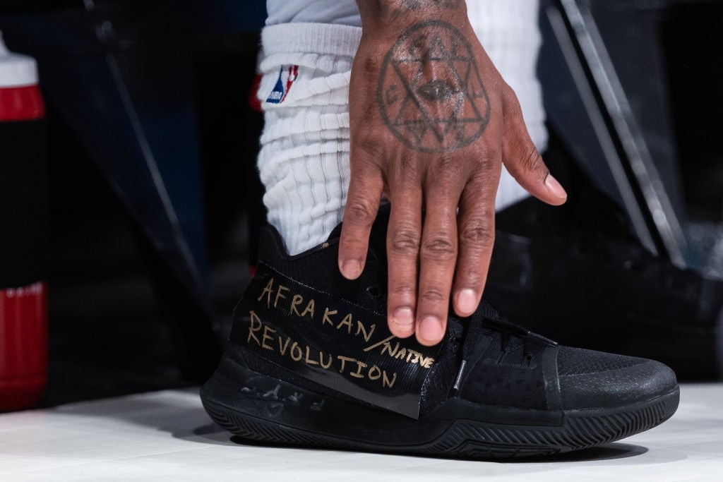 A manus  rests connected  a achromatic  sneaker with "Afrakan Native Revolution" written connected  it. The idiosyncratic   wears an NBA uniform