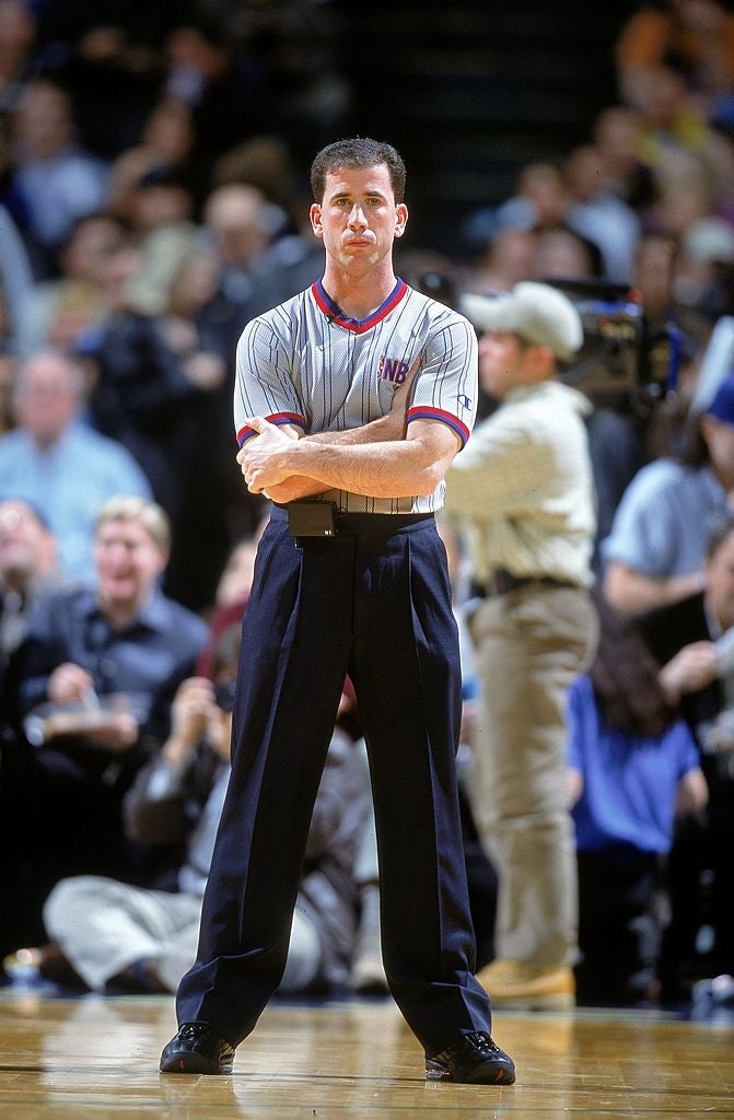Referee lasting  connected  a hoops  tribunal  during a game, wearing a striped referee azygous   with arms crossed, surrounded by a blurred crowd
