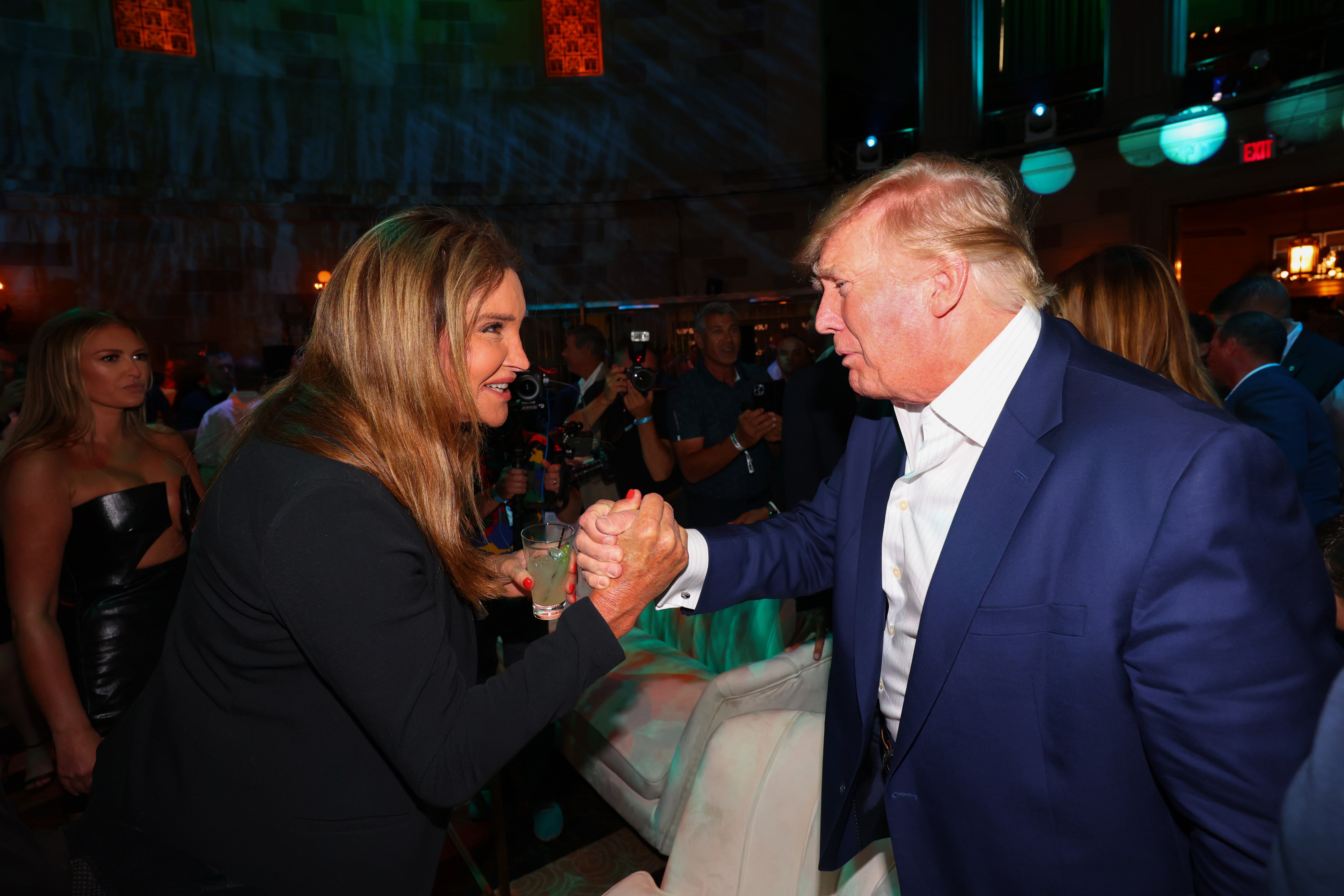 Caitlyn Jenner and Donald Trump shingle  hands surrounded by different   people