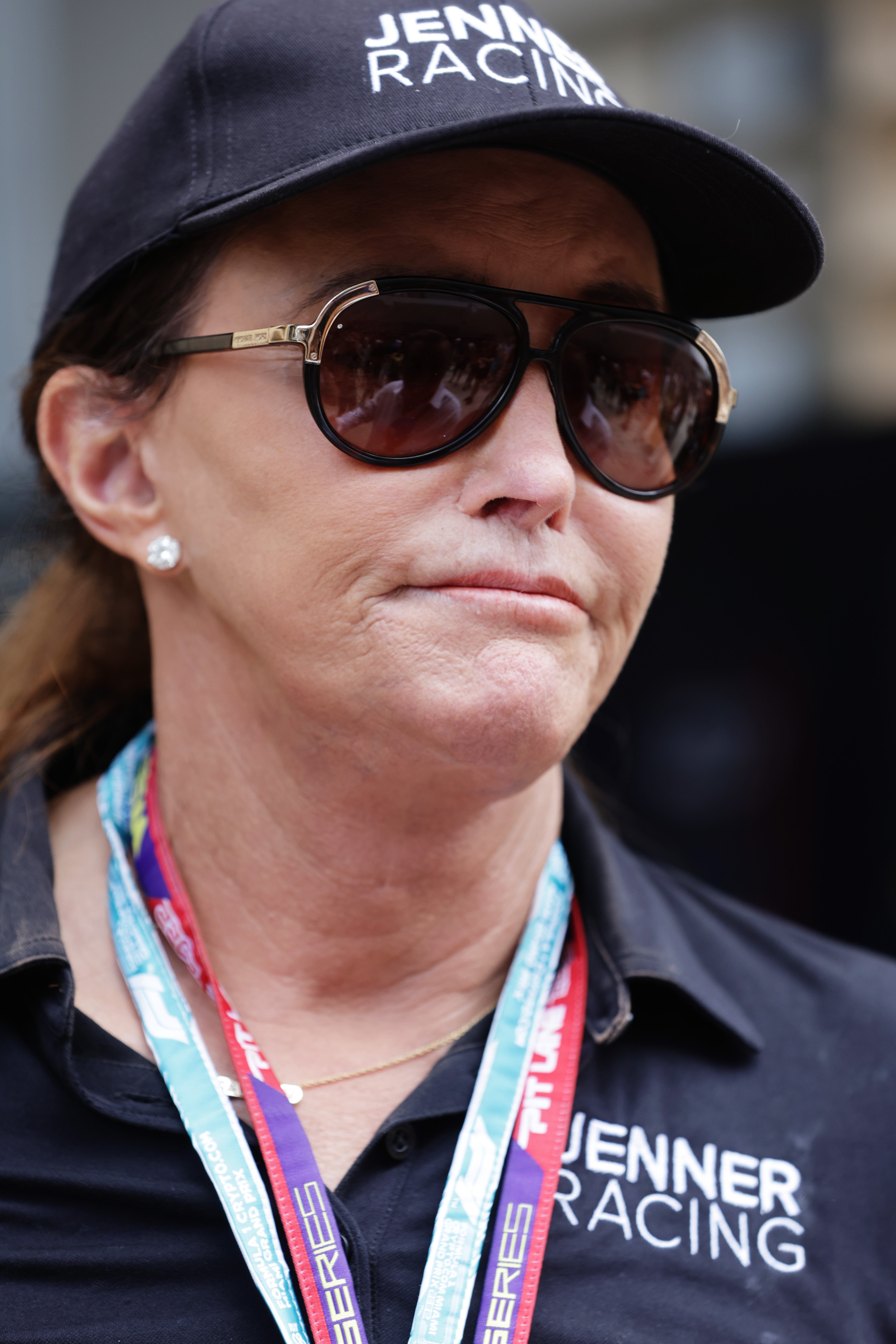 Caitlyn Jenner wearing a headdress  and sunglasses with branded text, attending a racing event, wearing a garment  with "Jenner Racing" text