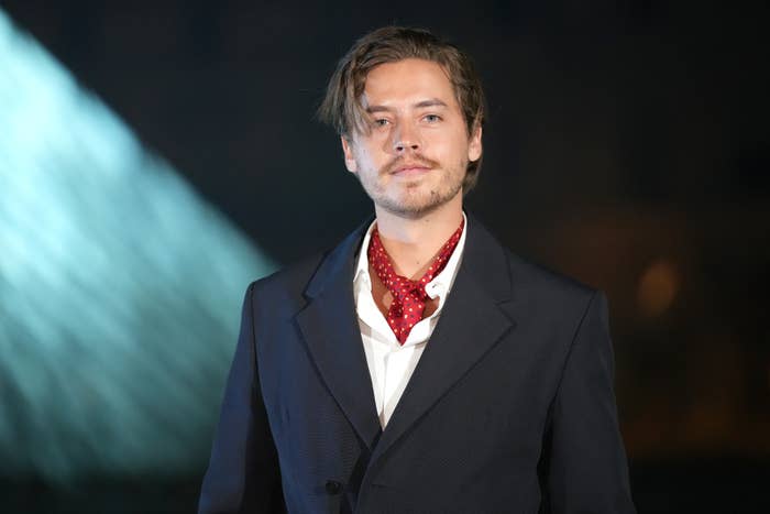 Dylan Sprouse successful  a crisp  suit   and scarf poses confidently astatine  a ceremonial  event