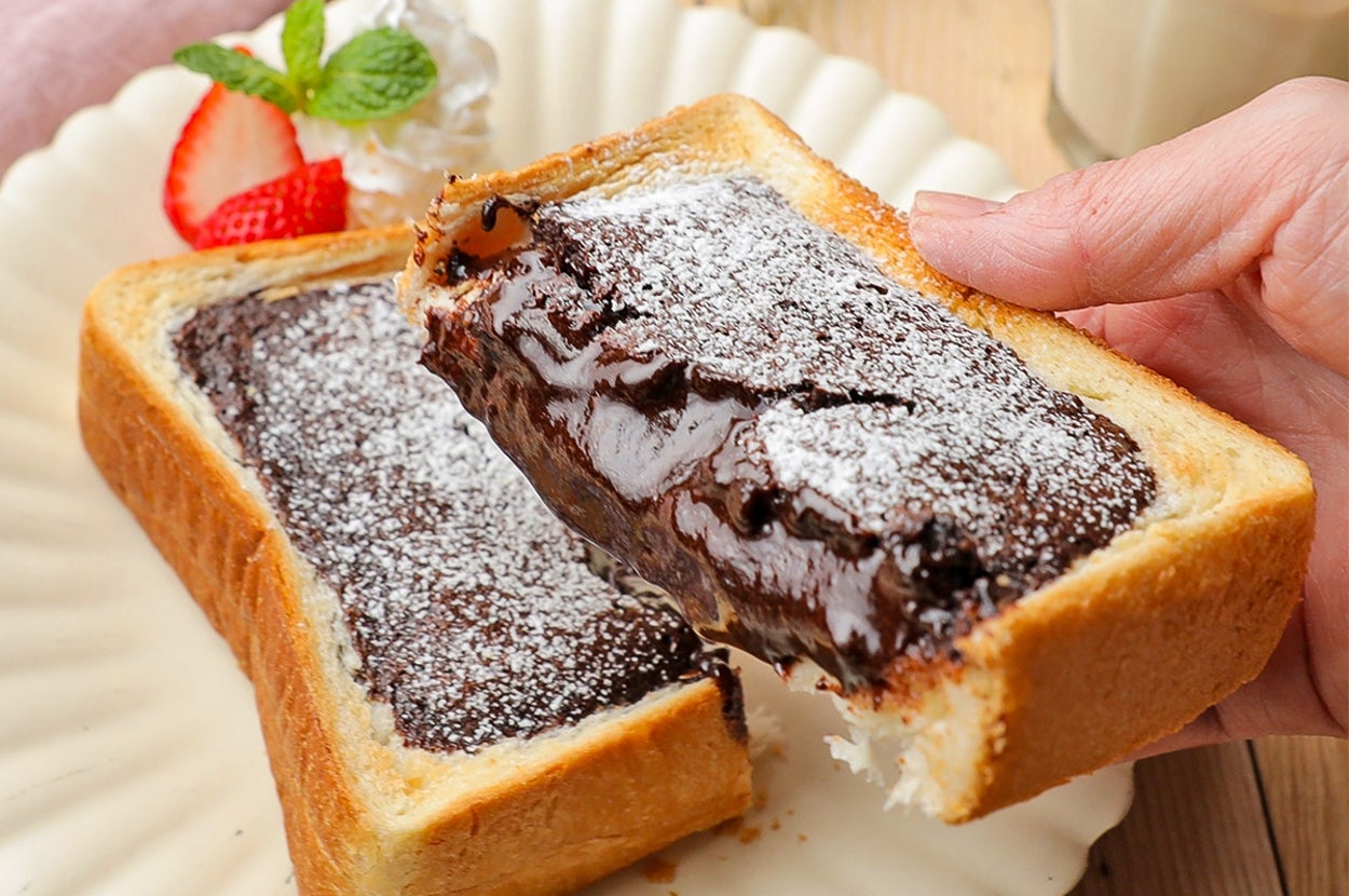 チョコレートトーストにパウダーシュガーがかかり、ストロベリーとミントが飾られている。手がトーストを持ち上げている。