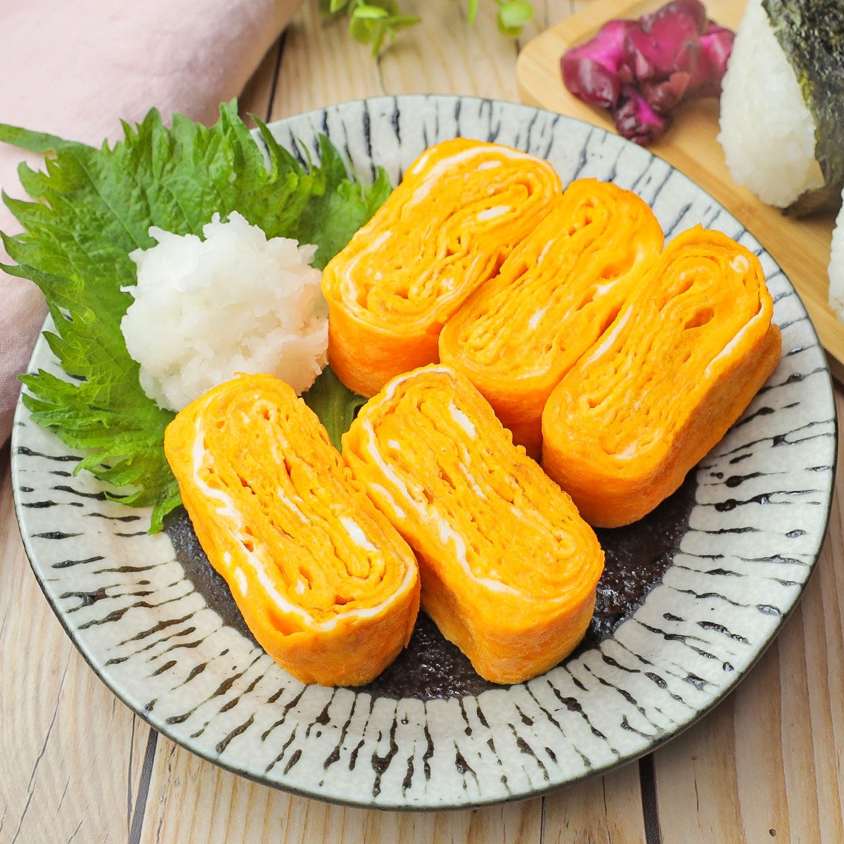 皿に盛られた厚焼き玉子の料理。大根おろしとシソの葉が添えられている。