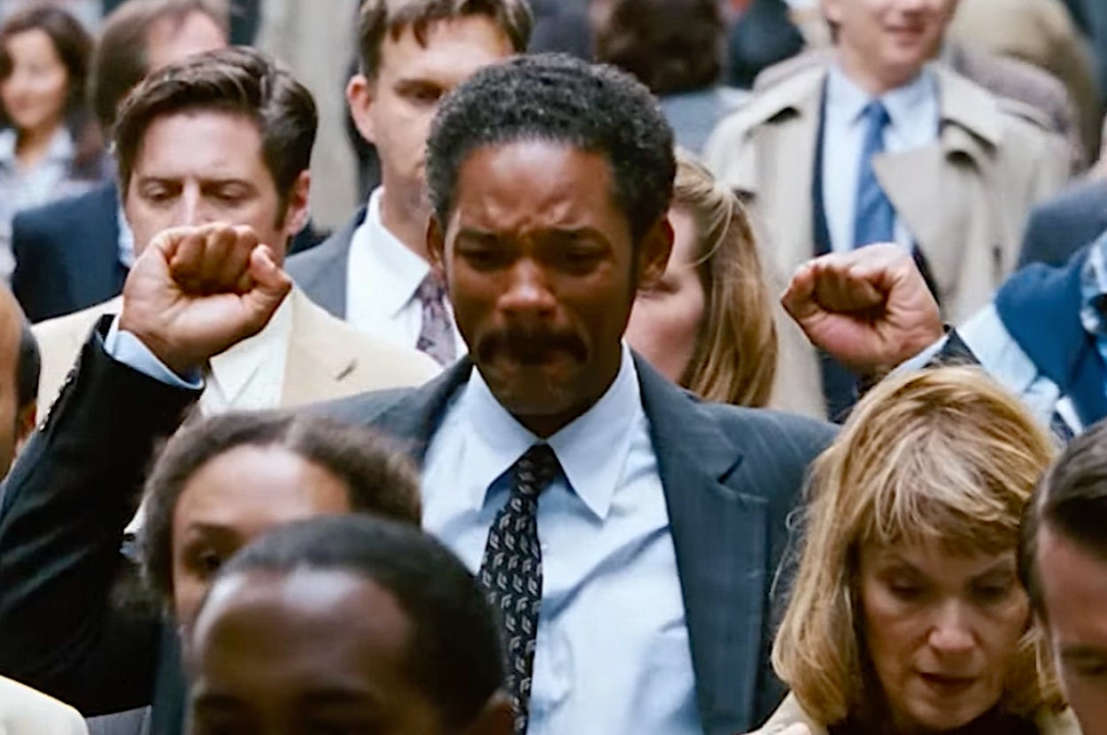 Will Smith in "The Pursuit of Happyness" in a suit with a patterned tie is walking amidst a crowd, raising his fists in a moment of triumph