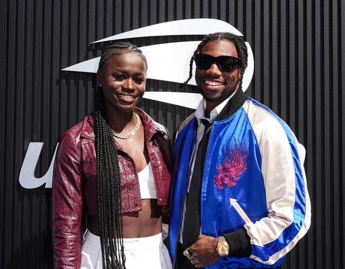 Two individuals smiling connected  a reddish  carpet. One is wearing a burgundy overgarment   implicit    a achromatic  outfit, and the different   a bluish  overgarment   with sunglasses