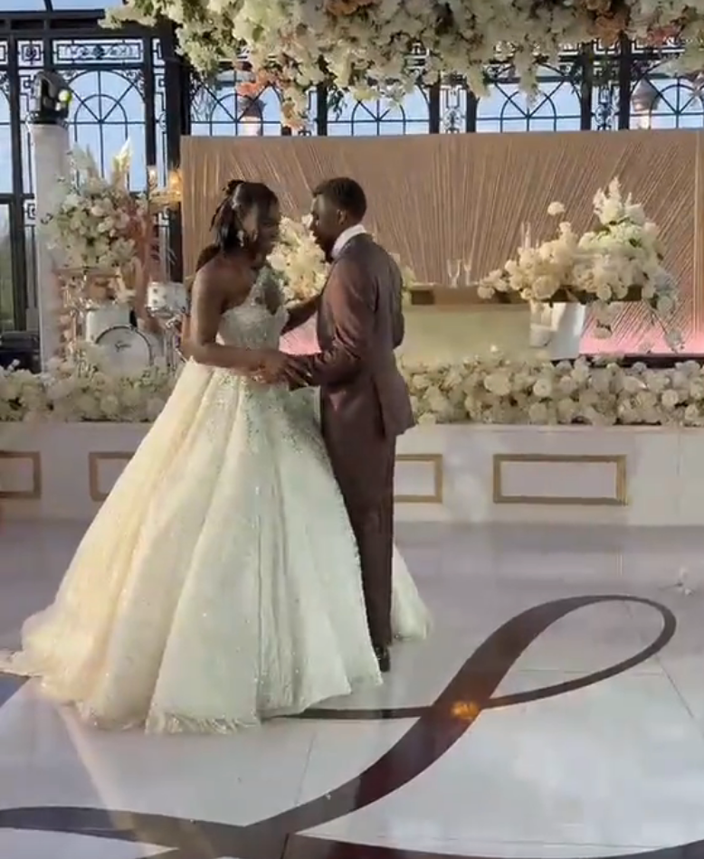A mates  dances astatine  a wedding reception, with the bride successful  an elegant shot  gown and the groom successful  a ceremonial  suit, surrounded by floral decor