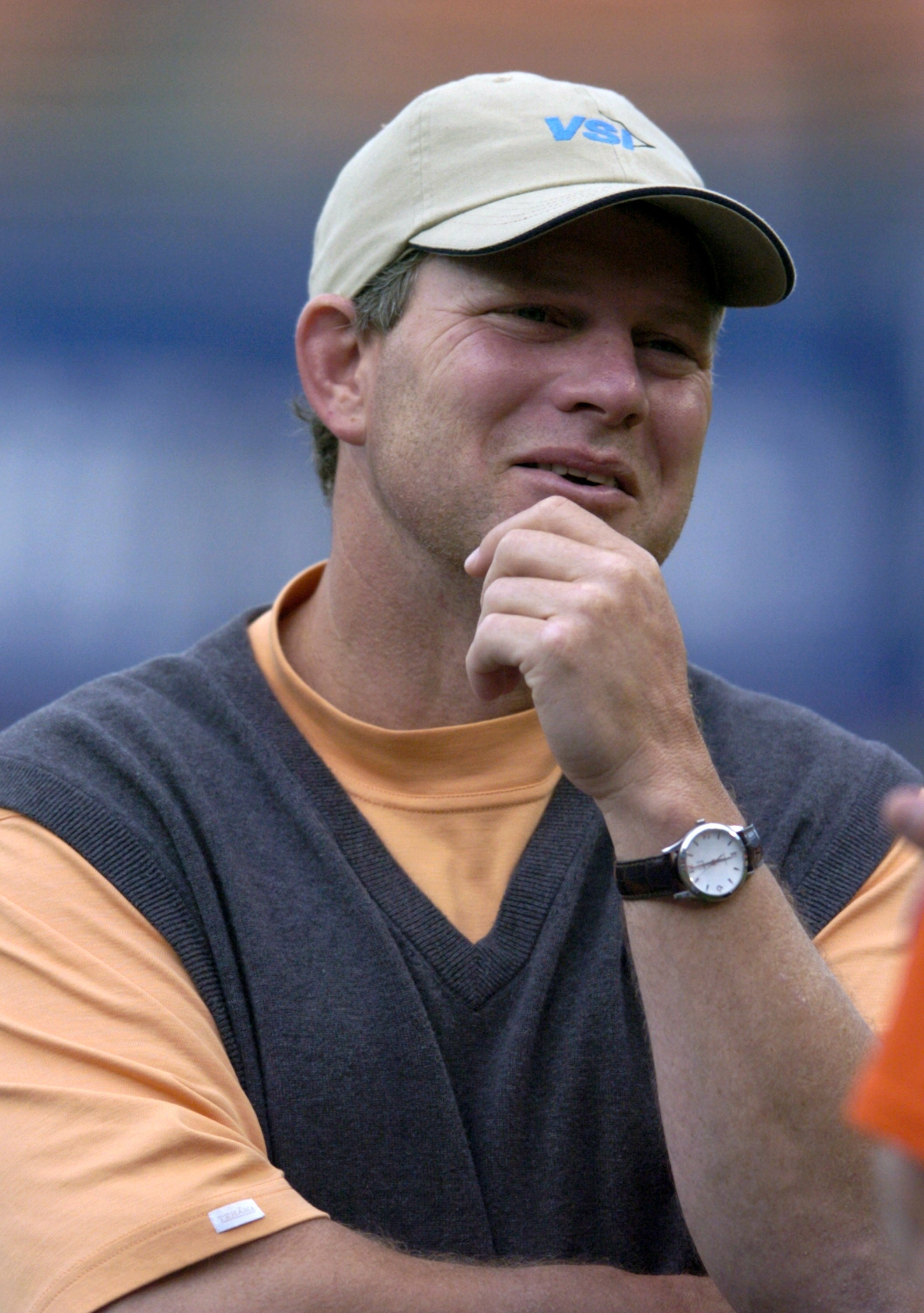 Person wearing a cap, casual shirt, and sweater vest, lasting  outdoors, appearing thoughtful