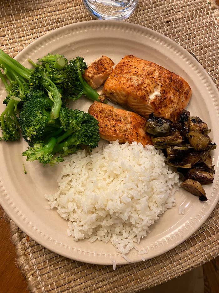 Plate with salmon, broccoli, rice, and roasted vegetables on a woven mat