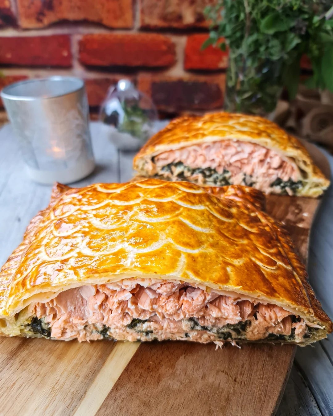 Pastry-wrapped salmon on a cutting board, showing flaked salmon filling with herbs. Candle and plants in background