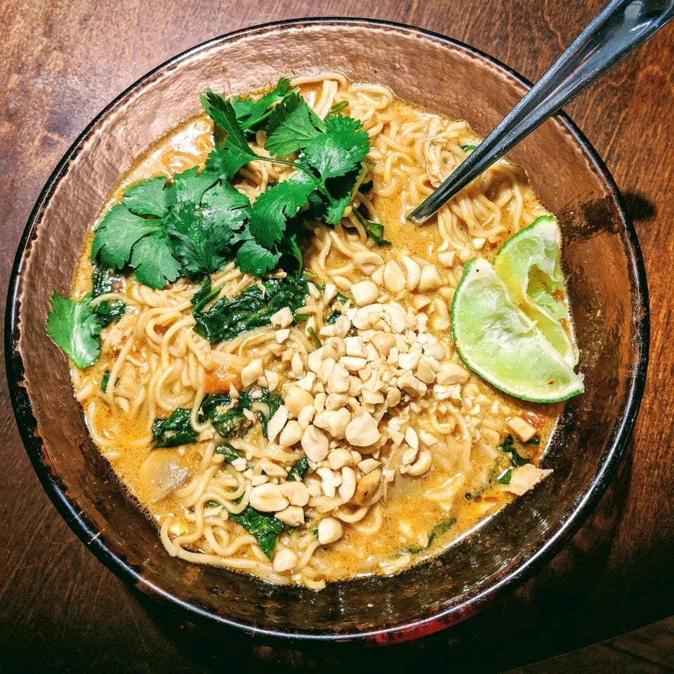 Bowl of ramen with cilantro, lime wedge, and peanuts on top, served with a fork