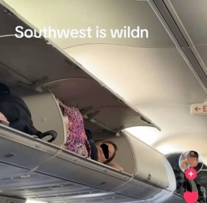 Person humorously lying inside an airplane's overhead compartment, with text "Southwest is wildn" overlayed