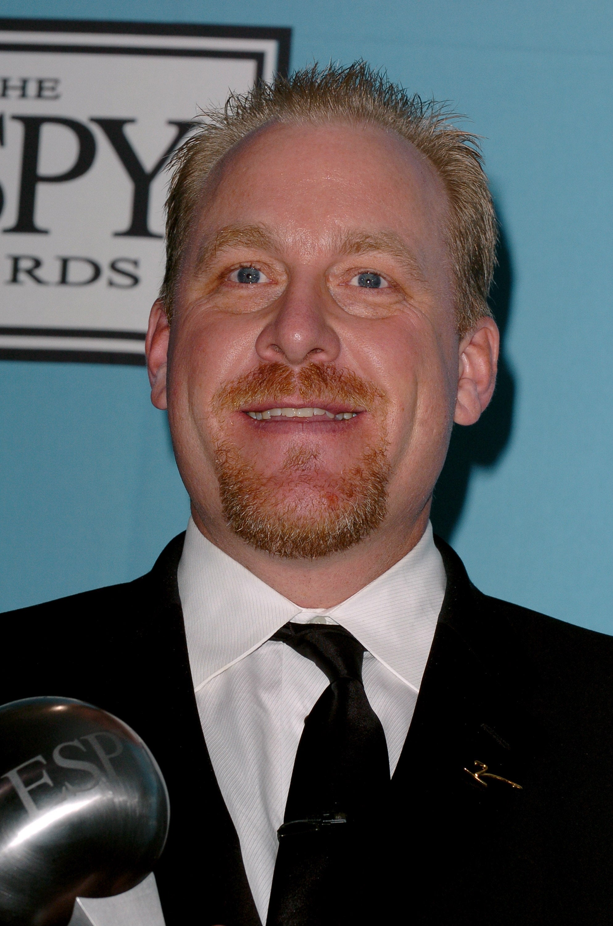 Smiling idiosyncratic   successful  a suit   and necktie  astatine  an event. The inheritance  includes a partial lawsuit   logo