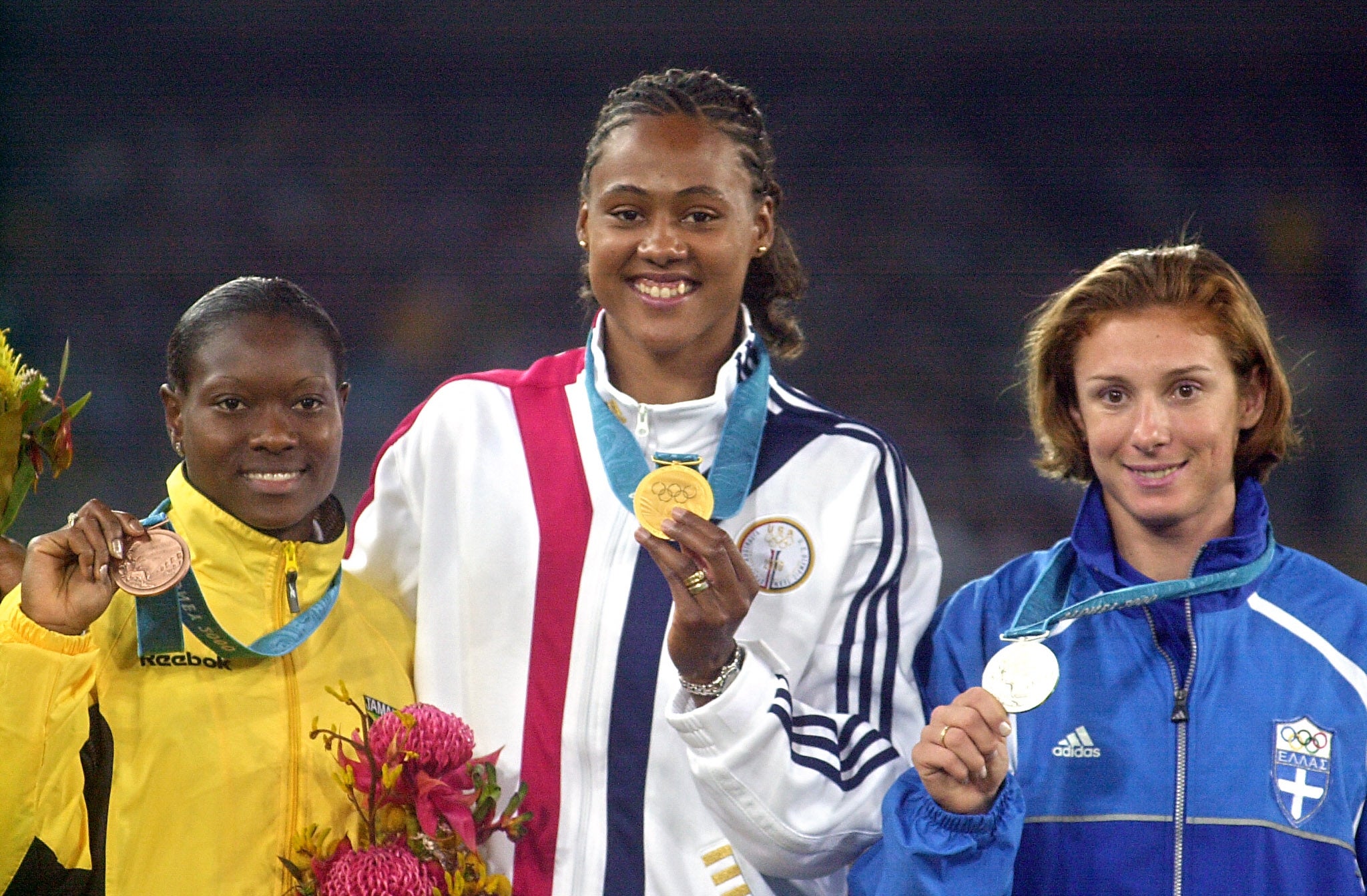 Three athletes basal   connected  a podium holding medals. They deterioration  tracksuits representing their countries