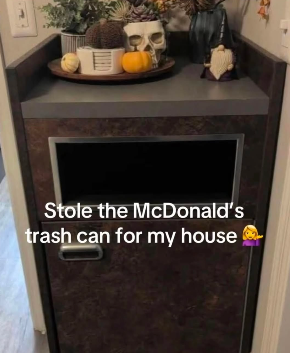 A McDonald's-style trash can is in a house, decorated with plants and pumpkins. Text on the image jokes about taking the trash can for home use
