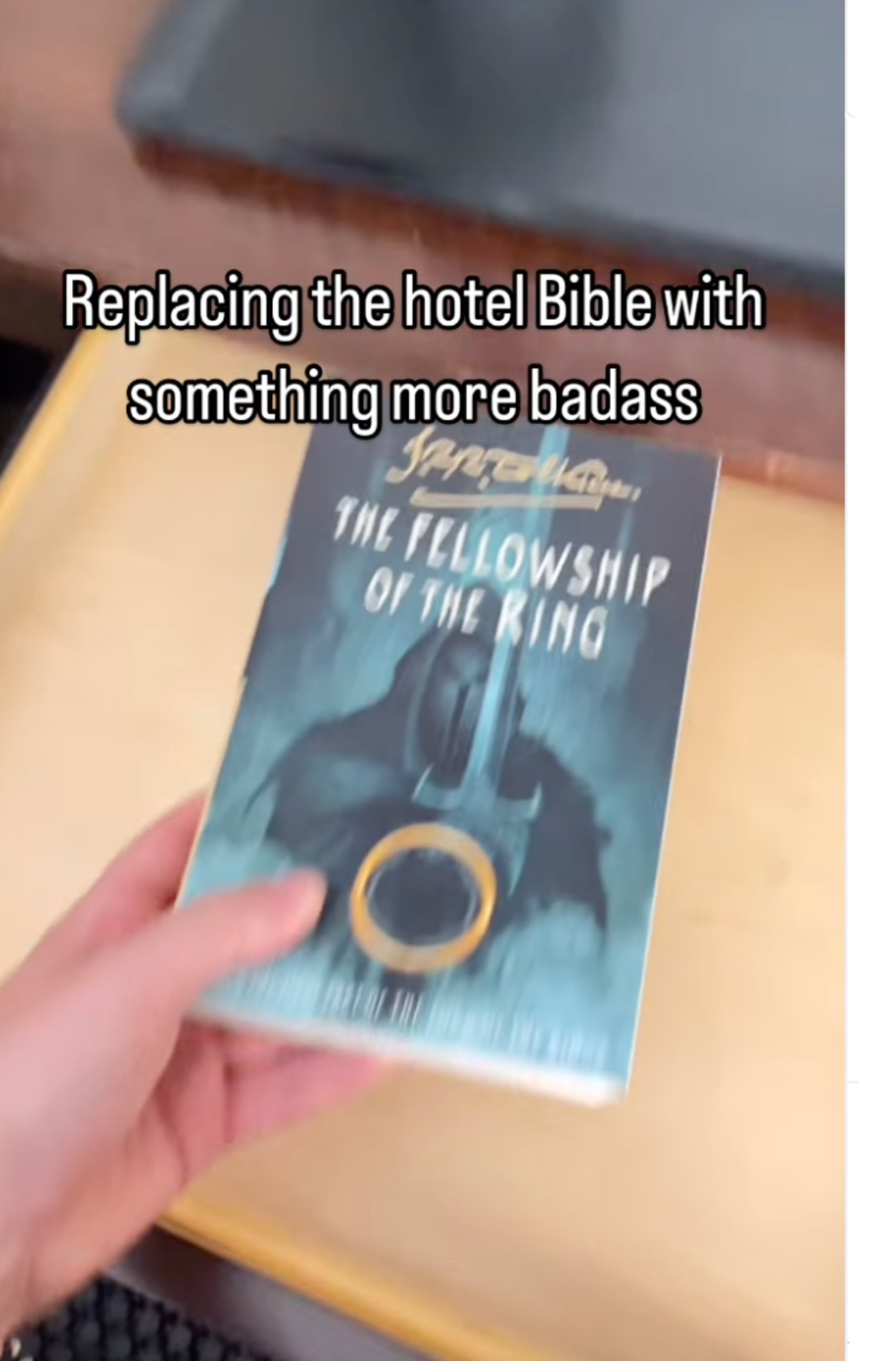 A hand places a copy of "The Fellowship of the Ring" book in a hotel drawer. Text reads: "Replacing the hotel Bible with something more badass."