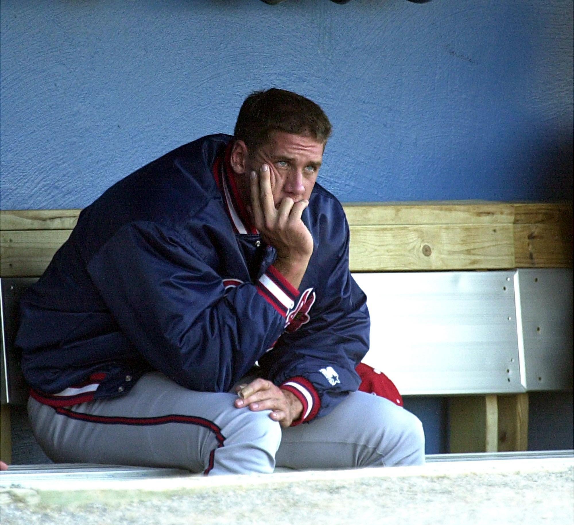 A idiosyncratic   successful  a shot   azygous   and overgarment   sits pensively connected  a seat  successful  a dugout, resting their look   connected  their hand