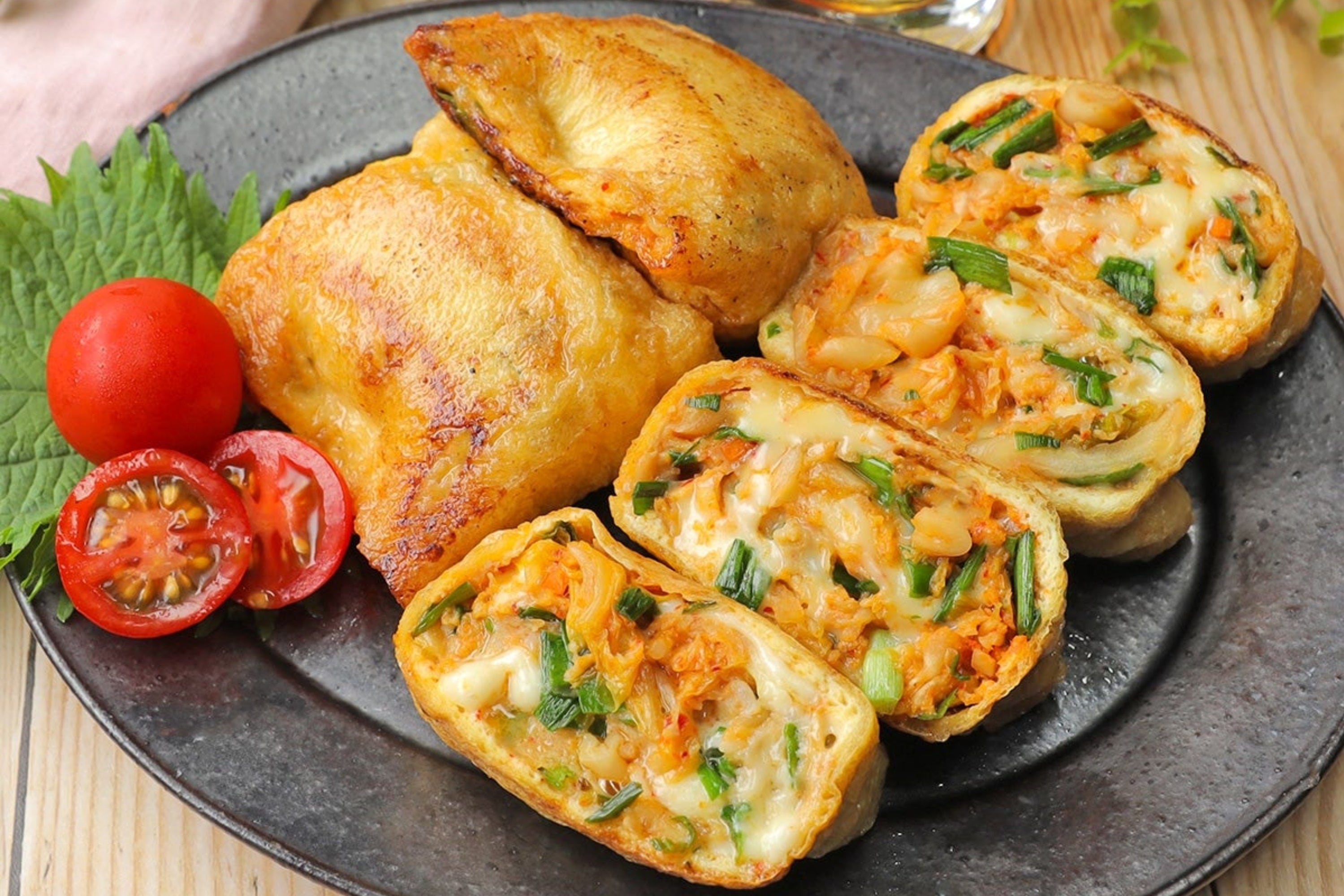 お皿に鶏肉と野菜やチーズが入ったカットロール、トマト、葉物とガラスの飲み物が置かれている食事風景。