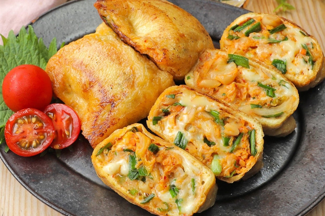 お皿に鶏肉と野菜やチーズが入ったカットロール、トマト、葉物とガラスの飲み物が置かれている食事風景。