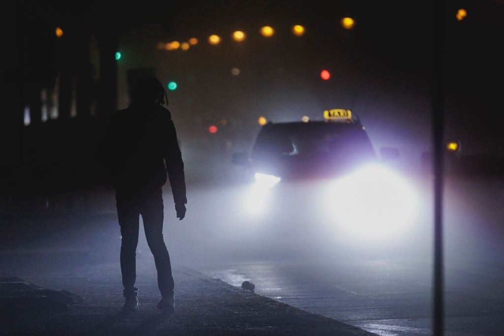 Person silhouetted successful  the thoroughfare  astatine  nighttime  arsenic  a taxi with headlights connected  approaches successful  the fog