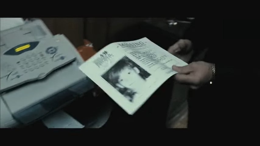 A idiosyncratic   holds a "Missing" poster with a photograph  and details of a missing child. A fax instrumentality   is disposable   beside them